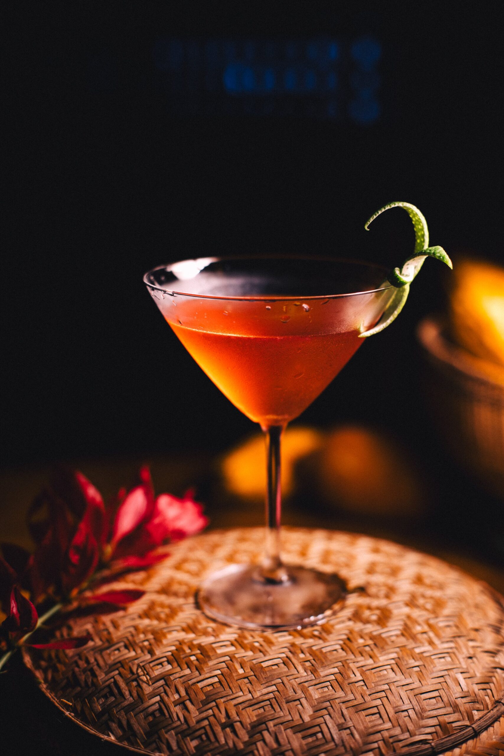 A deep red cocktail in a martini glass garnished with a lime twist, resting on a woven tray beside a red tropical flower at Anavilhanas Jungle Lodge Brazil