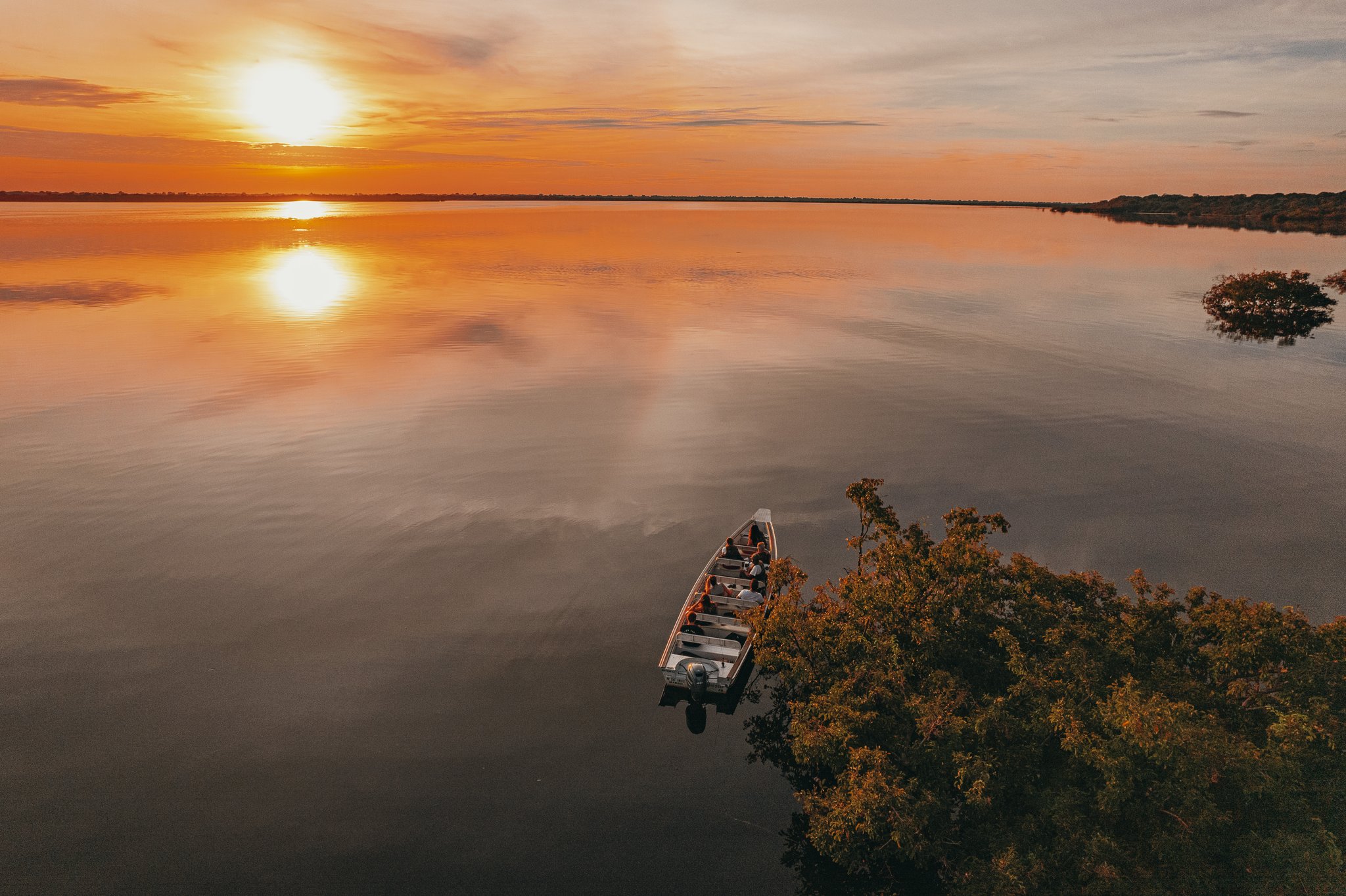 Aerial view of a small motorboat drifting on a mirror-still river at sunset, with the Anavilhanas Jungle Lodge Brazil region's golden sky reflected on the glassy black water
