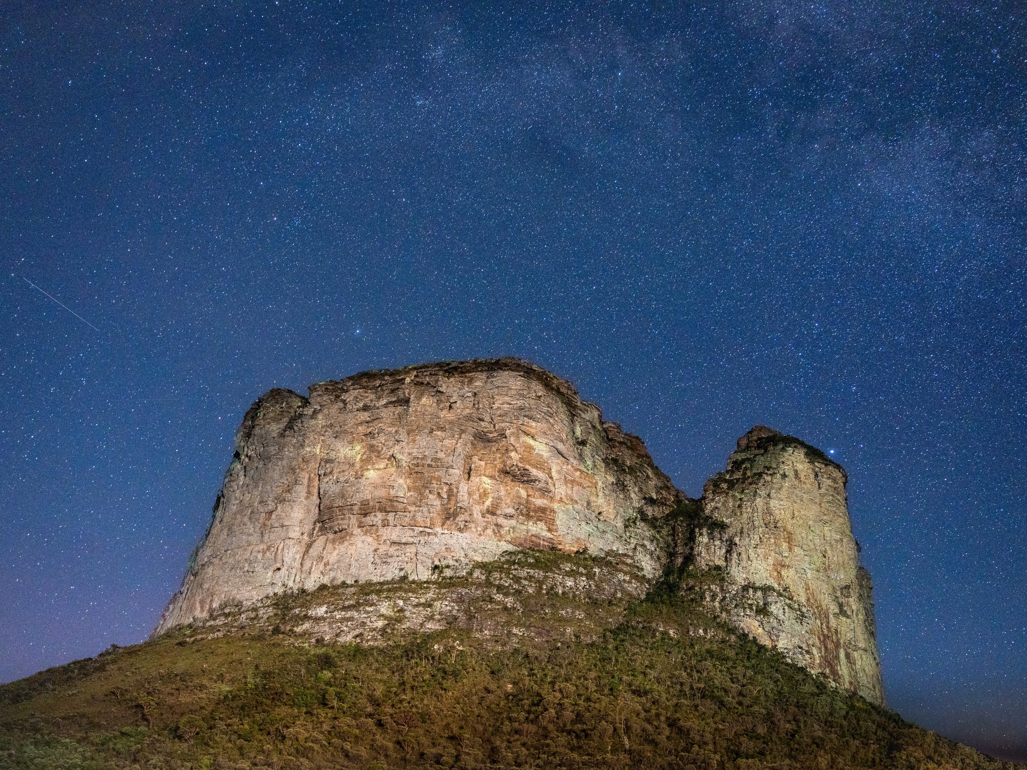 Massive sandstone rock formation in Chapada Diamantina tours region lit against a deep blue night sky filled with the Milky Way