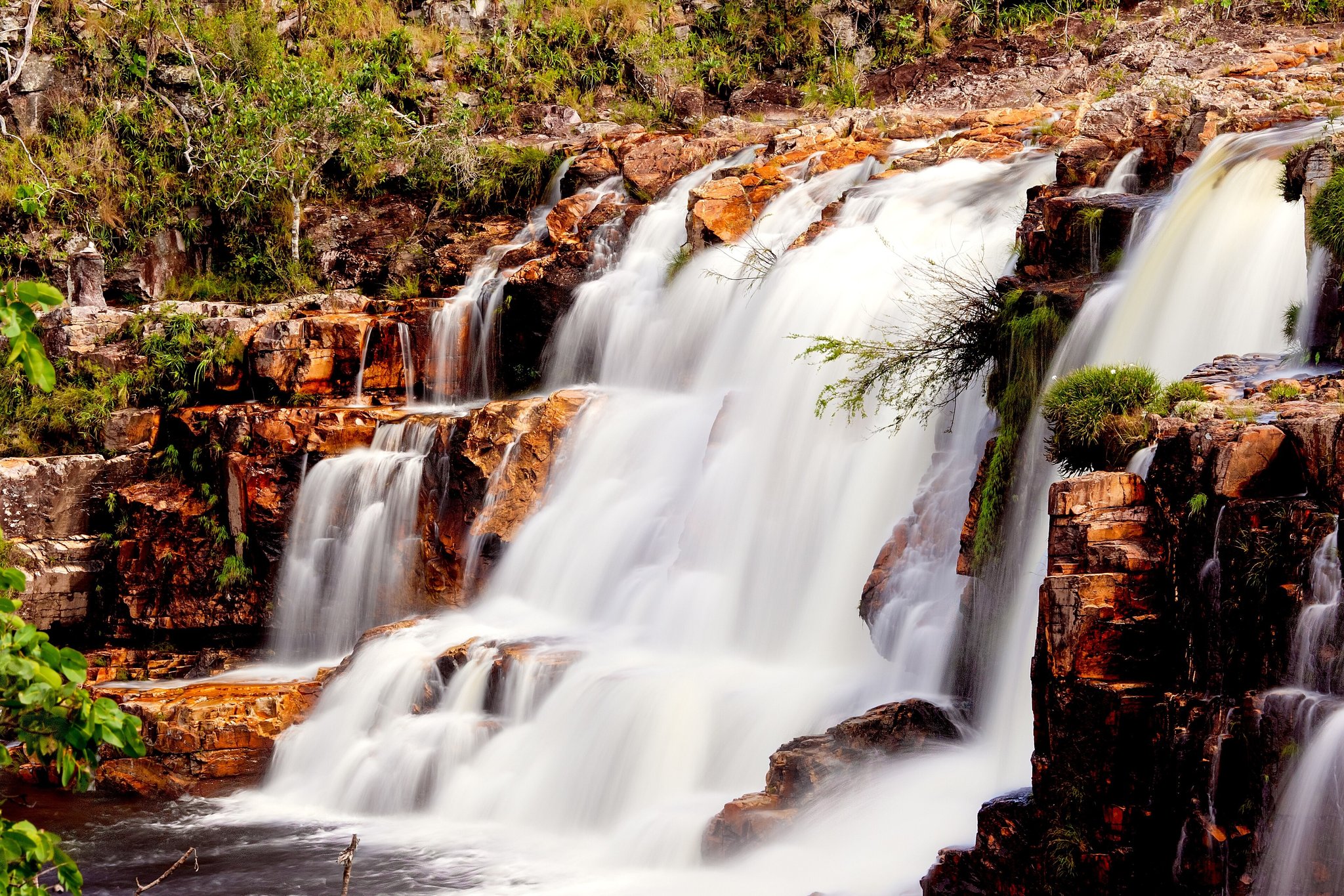 Cachoeira escalonada caindo sobre lajedos de quartzito ferrugem com vegetação do Cerrado nas trilhas da Chapada dos Veadeiros