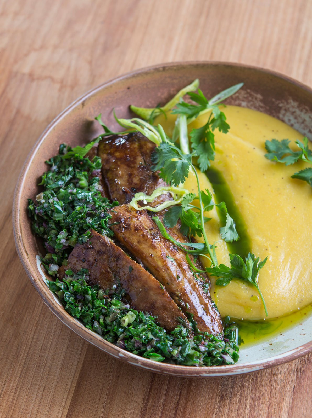Caramelised plantain, herb salsa, golden purée — dinner in the heart of the Amazon. Photo: Rjcastilho A rustic ceramic bowl at Cristalino Jungle Lodge holding caramelised plantain slices, vibrant herb salsa, and a smooth golden purée garnished with fresh coriander