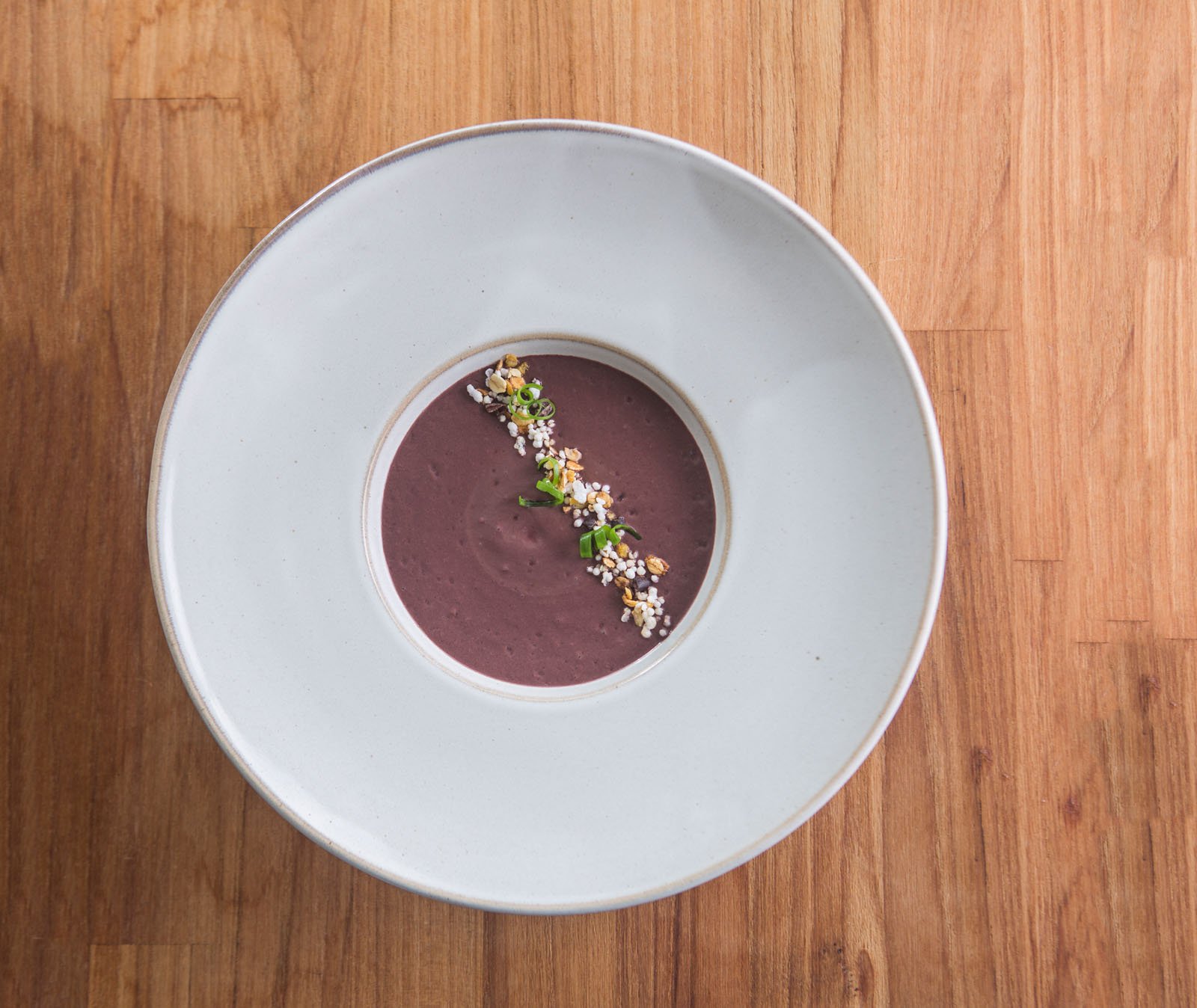 Forest ingredients, plated with quiet precision. Photo: Rjcastilho A smooth deep-purple cream soup served in a wide white ceramic bowl at Cristalino Jungle Lodge, garnished with a diagonal line of toasted grains, puffed seeds, and sliced spring onion