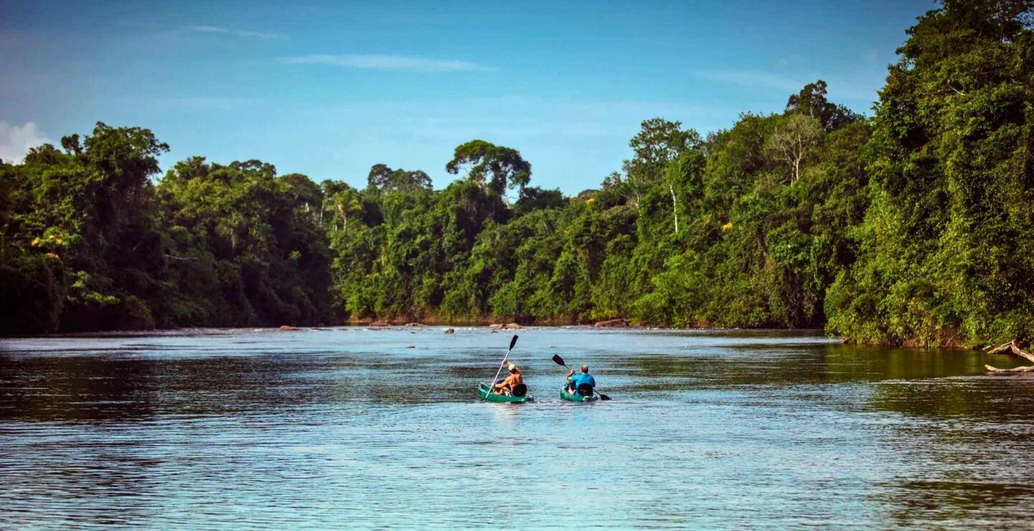 Two kayakers paddling side by side on a wide river flanked by dense Amazon rainforest at Cristalino Jungle Lodge