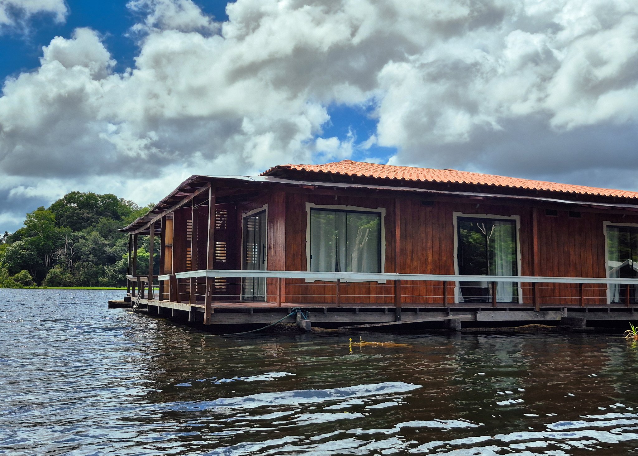 Full wooden facade of the Eco Floating Lodge stretching along the water under a cloudy sky