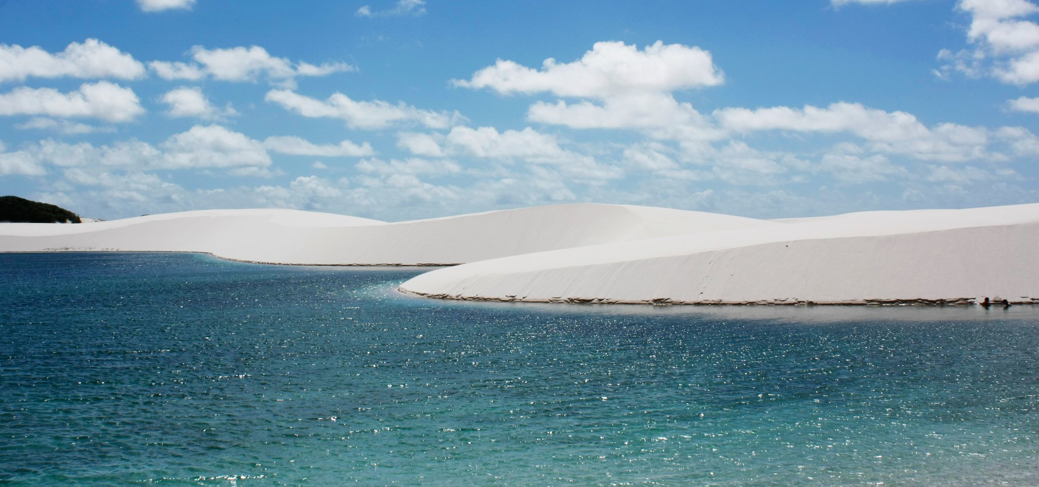 Crystal-clear blue lagoon reflecting a brilliant sky, framed by sweeping white sand dunes — the iconic landscape of the horseback riding Lençóis Maranhenses tour
