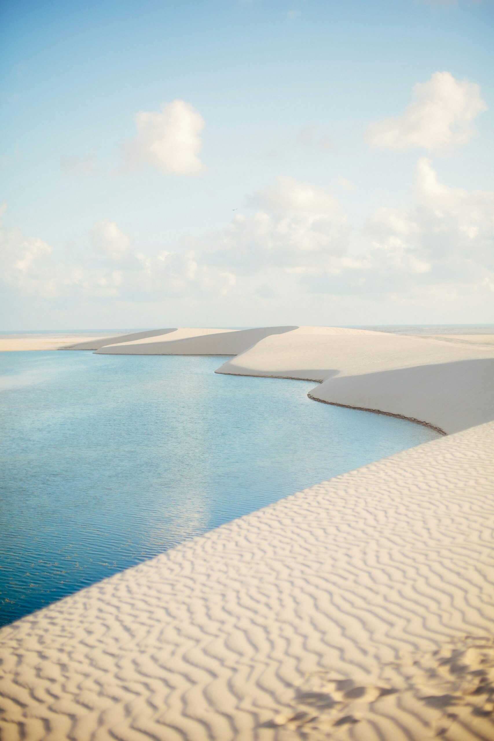 Turquoise rainwater lagoon nestled between sweeping white sand dunes under a soft blue sky in Lençóis Maranhenses, a highlight of the horseback riding Lençóis Maranhenses tour