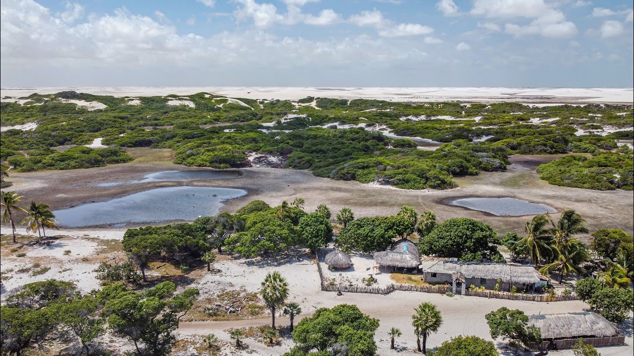 Aerial view of a small thatched-roof village nestled among white sand dunes, scrub vegetation and shallow lagoons on the horseback riding Lençóis Maranhenses tour route