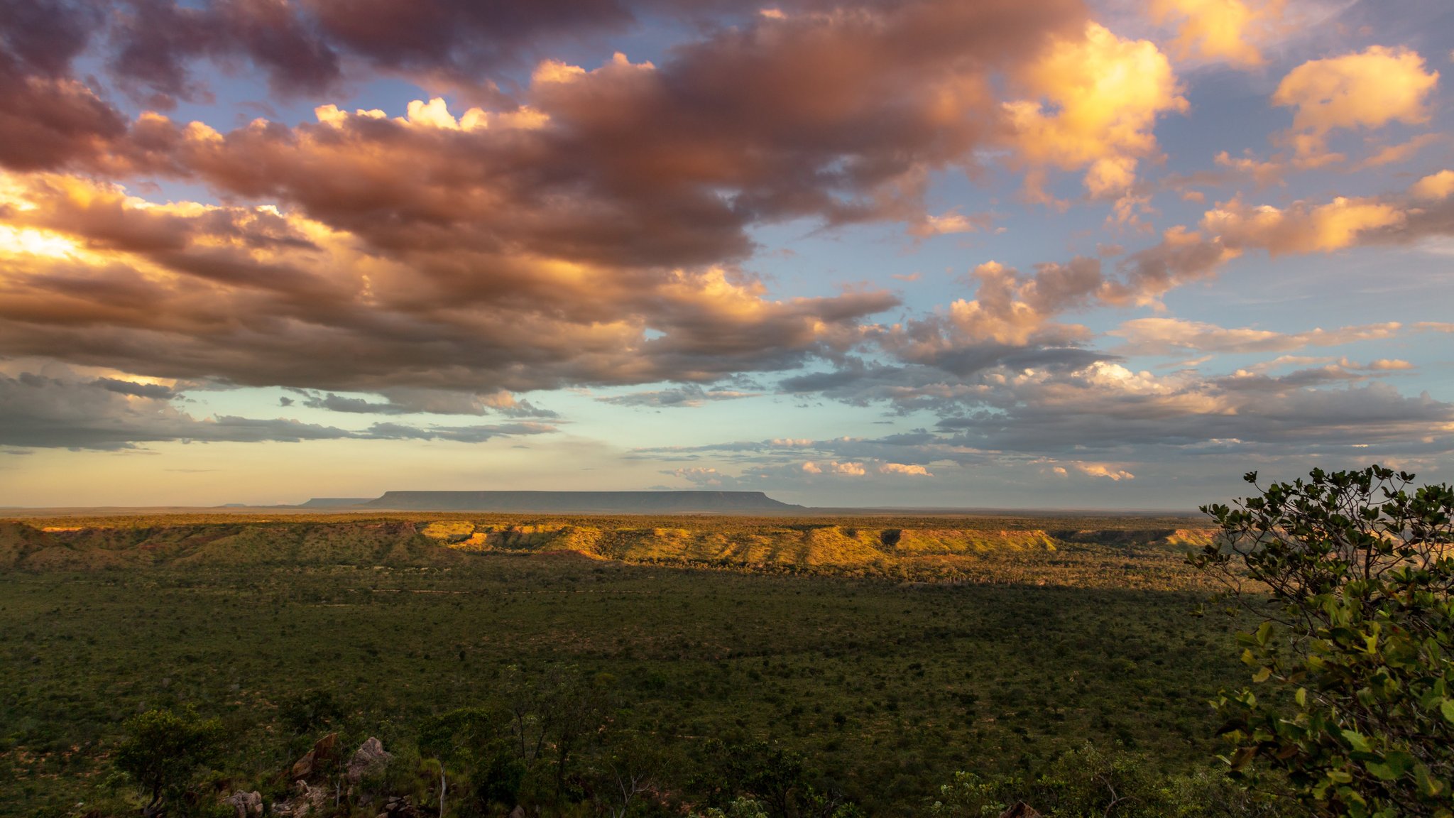 Een weids Cerrado-landschap bij zonsondergang tijdens een Jalapão-avontuur, met een tafelberg als silhouet tegen een dramatische hemel van gouden en roze wolken