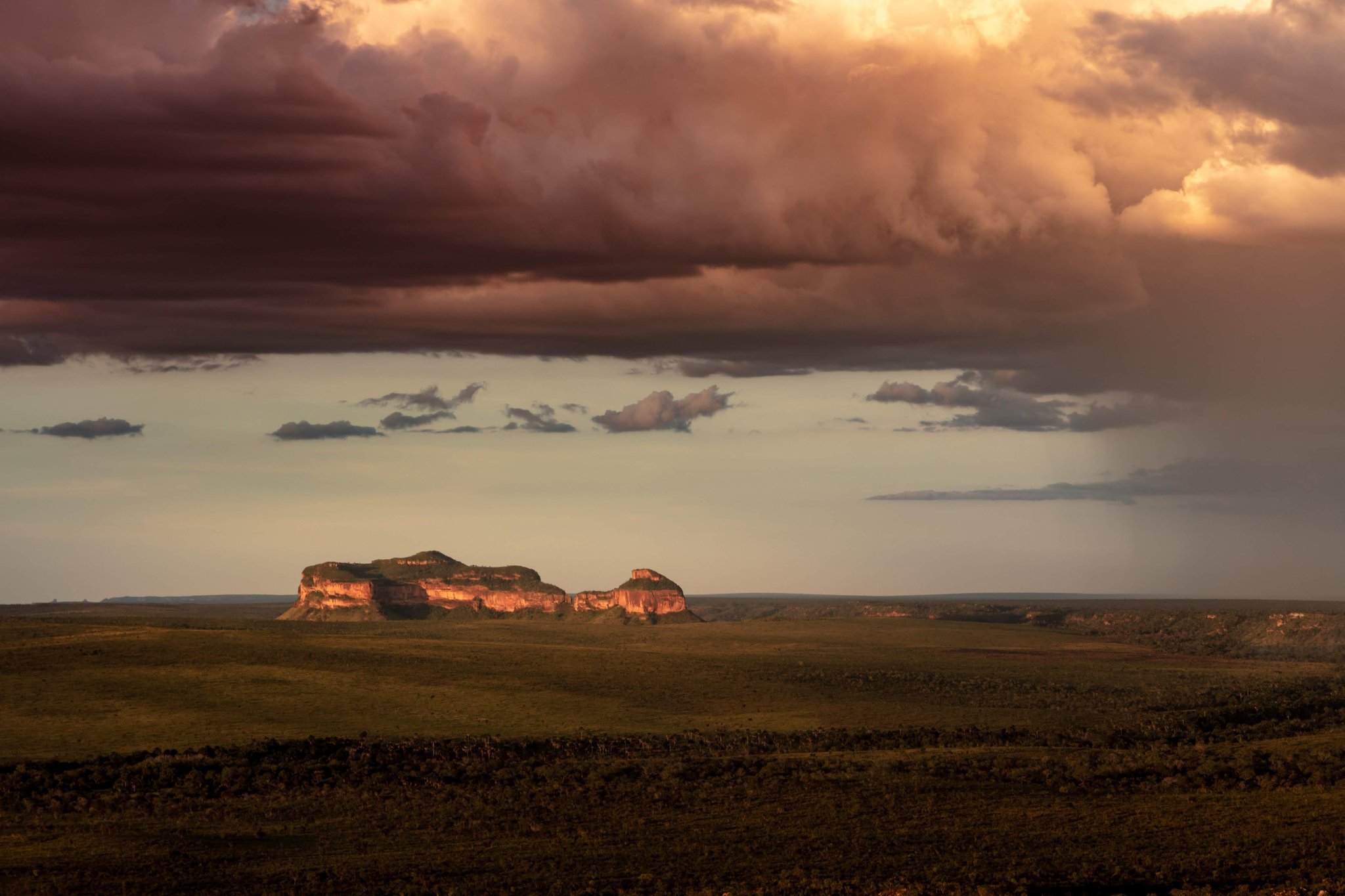 Twee vlakke zandsteen-mesas gloeien amberkleurig in het laatste licht terwijl een dramatisch onweersfront over de open Cerrado-vlakte trekt tijdens een Jalapão-avontuur
