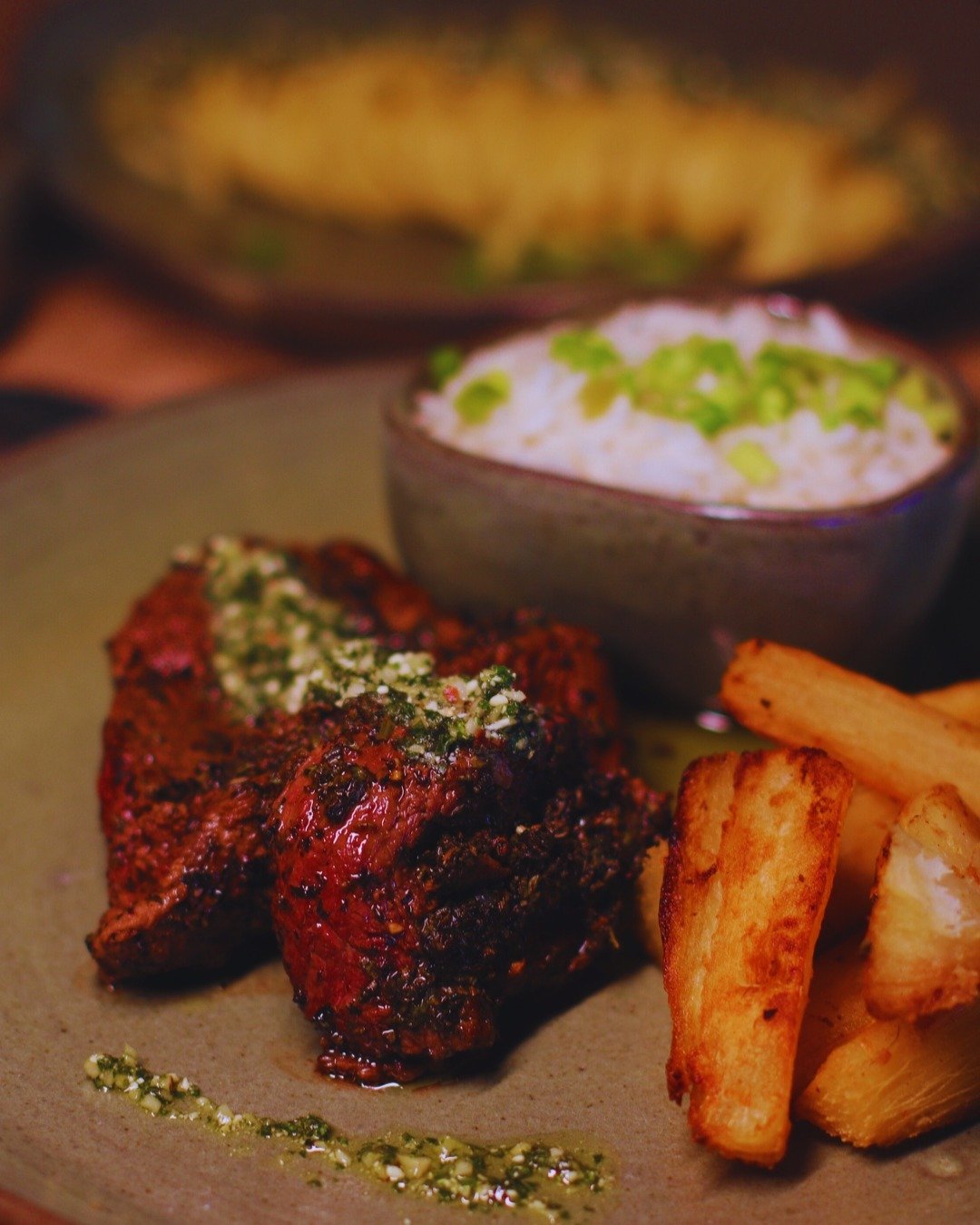 Herb-crusted, fire-kissed, and plated with pride — dinner at the heart of the Amazon. A herb-crusted grilled meat fillet topped with chimichurri, served with fried cassava sticks and a bowl of white rice with spring onions at Juma Amazon Jungle Lodge