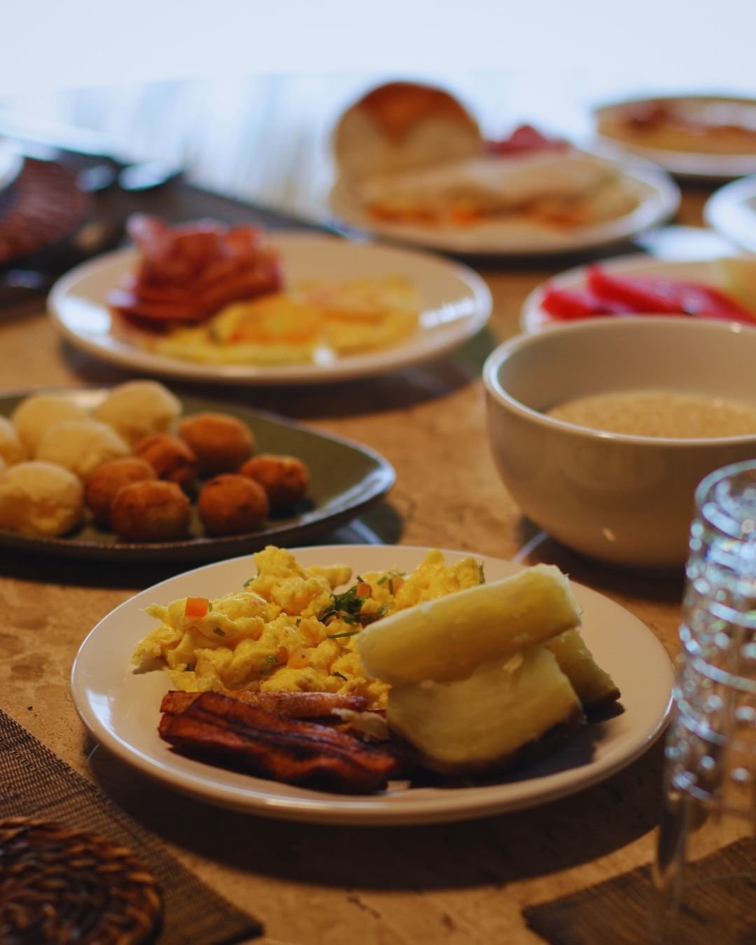 Ein reichhaltiges Frühstücksbuffet in der Juma Amazon Jungle Lodge mit Rühreiern, knusprigem Speck, gekochtem Maniok, gepökeltem Fleisch, frischer roter Paprika, gebratenem Gebäck, Brötchen und einem Schälchen Brei auf einem Holztisch