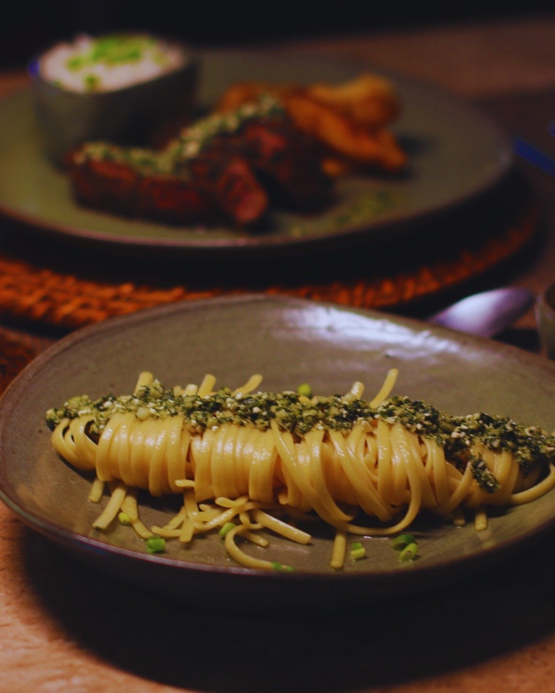 Ein Nest aus Linguine-Pasta mit Kräuter- und Saatenkruste auf einem rustikalen Keramikteller in der Juma Amazon Jungle Lodge, im Hintergrund verschwommen ein Teller mit gegrilltem Fleisch