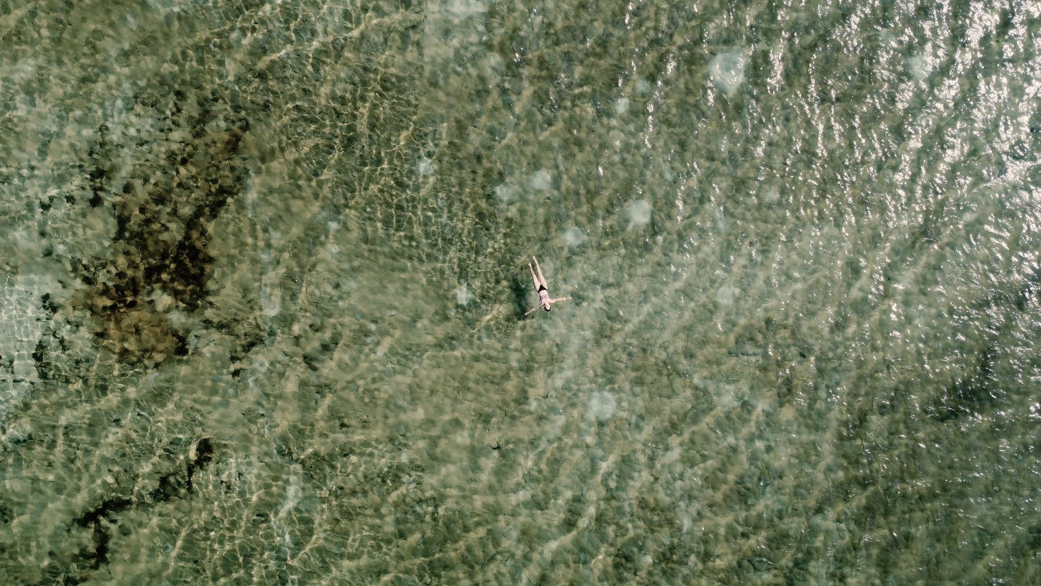 Sozinho numa lagoa transparente, entre o céu e a areia branca. Vista aérea de um nadador solitário flutuando nas águas rasas e cristalinas de uma lagoa durante a travessia dos Lençóis Maranhenses, com o fundo de areia visível através da superfície
