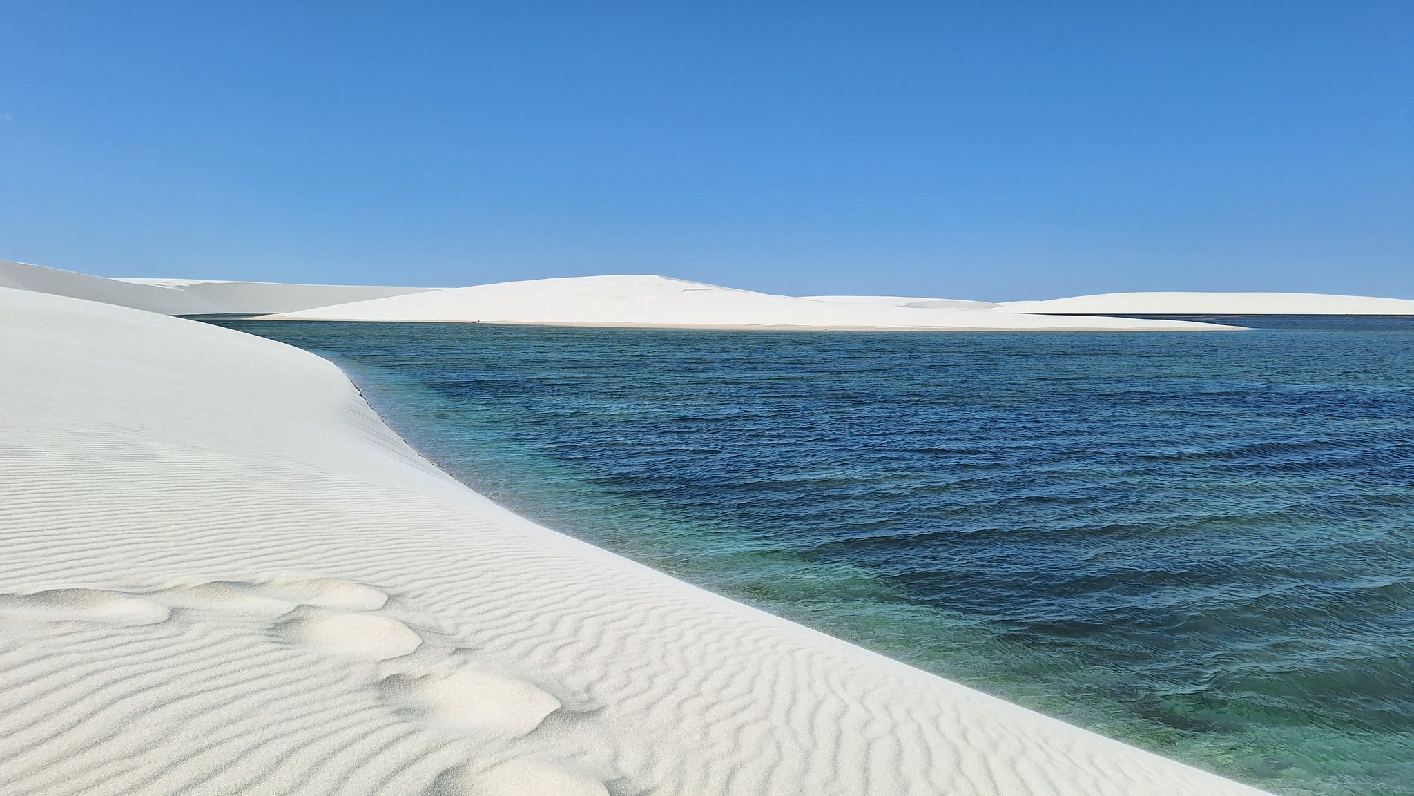 Areia branca, água fria e um horizonte sem fim. Lagoa turquesa de águas cristalinas emoldurada por extensas dunas de areia branca e céu azul intenso nos Lençóis Maranhenses