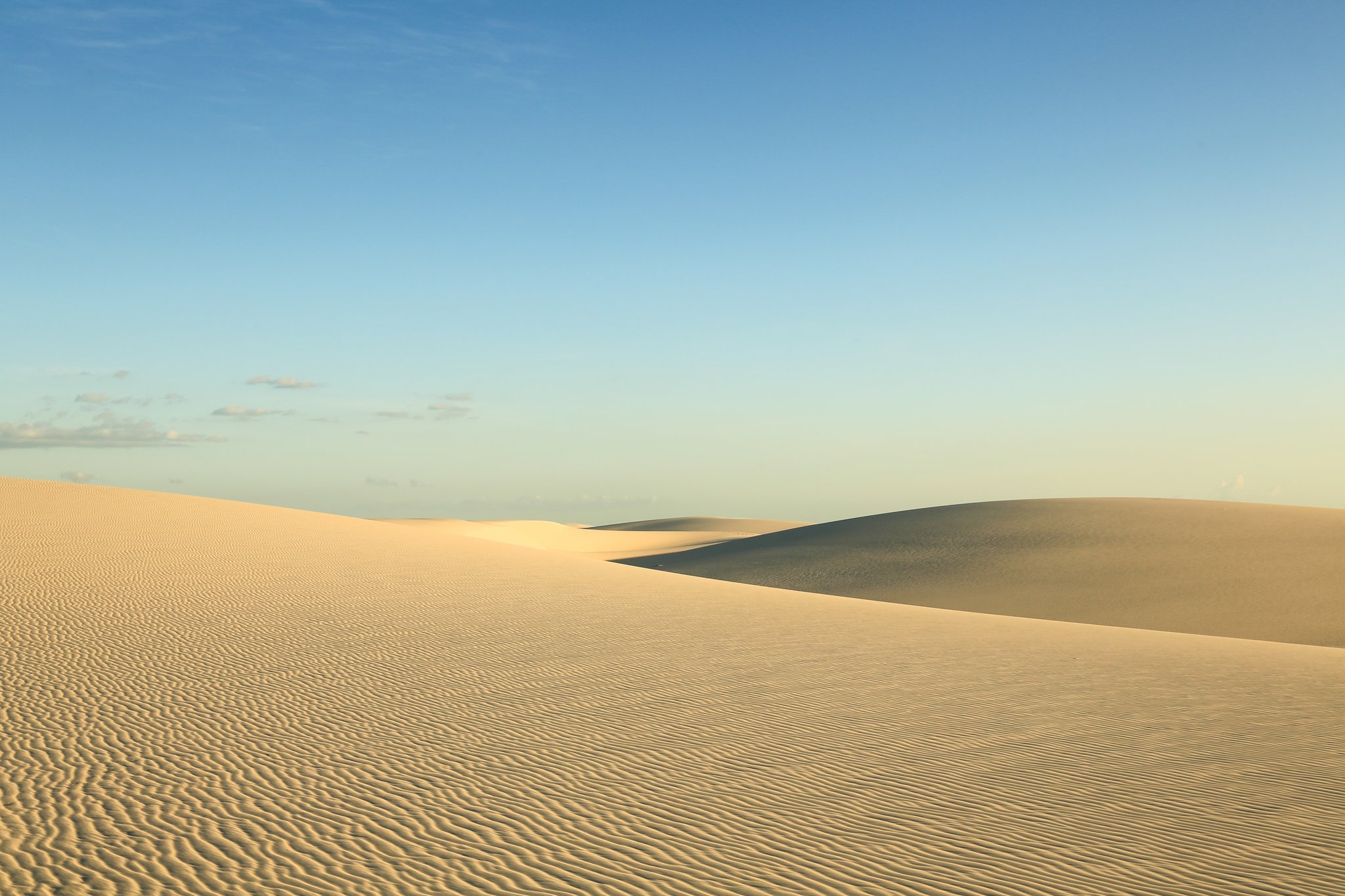 Cumes moldados pelo vento, silêncio absoluto — as dunas em sua forma mais pura. Photo: Brunomsbarreto Imensas dunas de areia branca sob céu azul claro durante a caminhada pelos Lençóis Maranhenses, com cumes rippled pelo vento até o horizonte