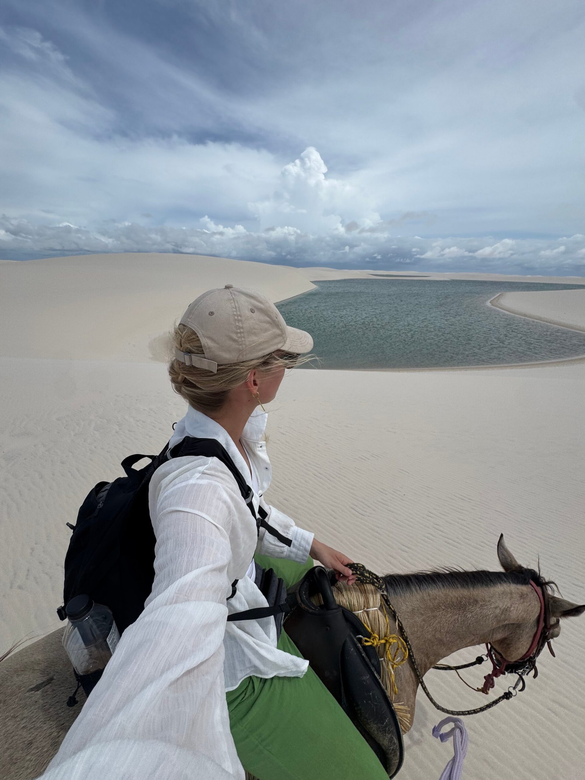 A rider stands beside her horse on the dunes, looking out over a lagoon in the roadless interior of Lençóis Maranhenses.