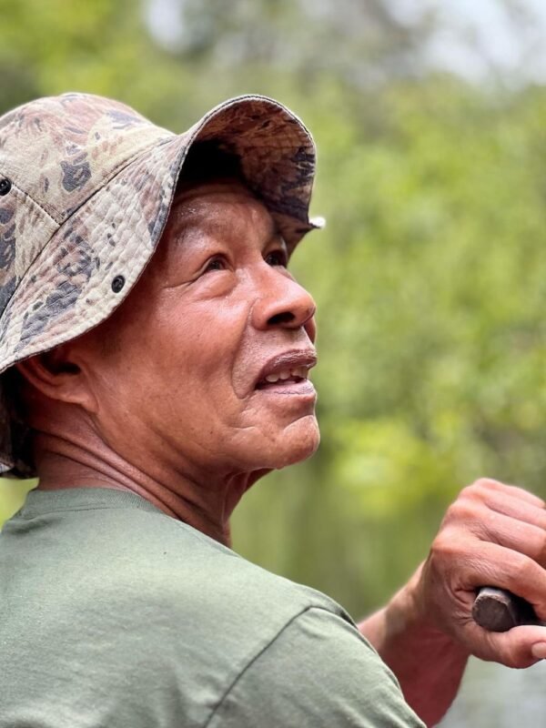 The local guides carry generations of forest knowledge in every story. Portrait of a local Amazon guide in a camouflage bucket hat looking into the distance