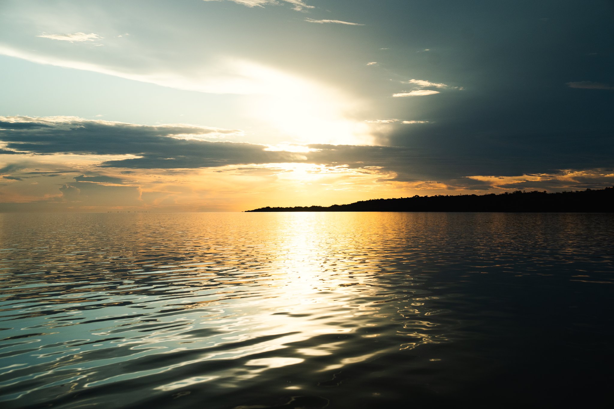 Pôr do sol dourado refletido sobre as águas calmas de um grande rio durante um cruzeiro de luxo pelo Amazonas no Brasil, com a silhueta de uma ilha coberta de floresta no horizonte