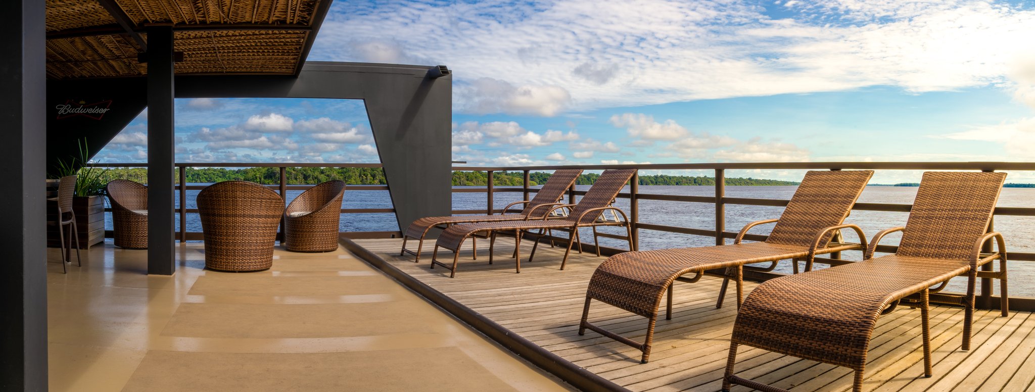 Espreguiçadeiras e cadeiras de vime no deck superior de um cruzeiro de luxo na Amazônia brasileira, com vista para um amplo rio de águas negras margeado por floresta tropical densa