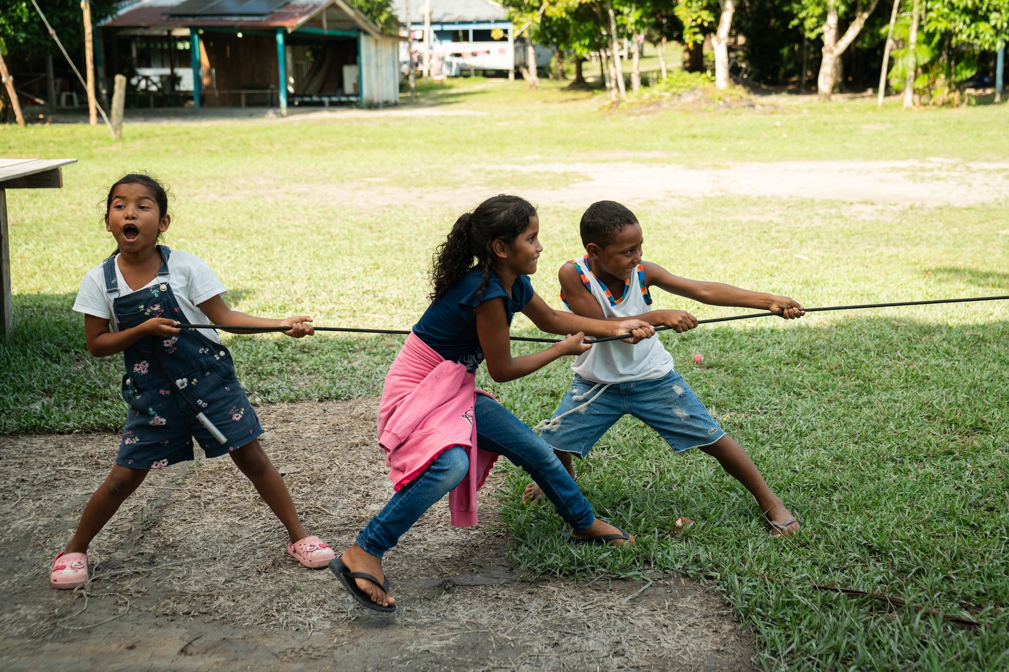 Três crianças riem e puxam uma corda com toda a força em uma brincadeira de cabo de guerra em um vilarejo ribeirinho, um momento inesquecível das visitas comunitárias durante um cruzeiro de luxo pelo Amazonas no Brasil