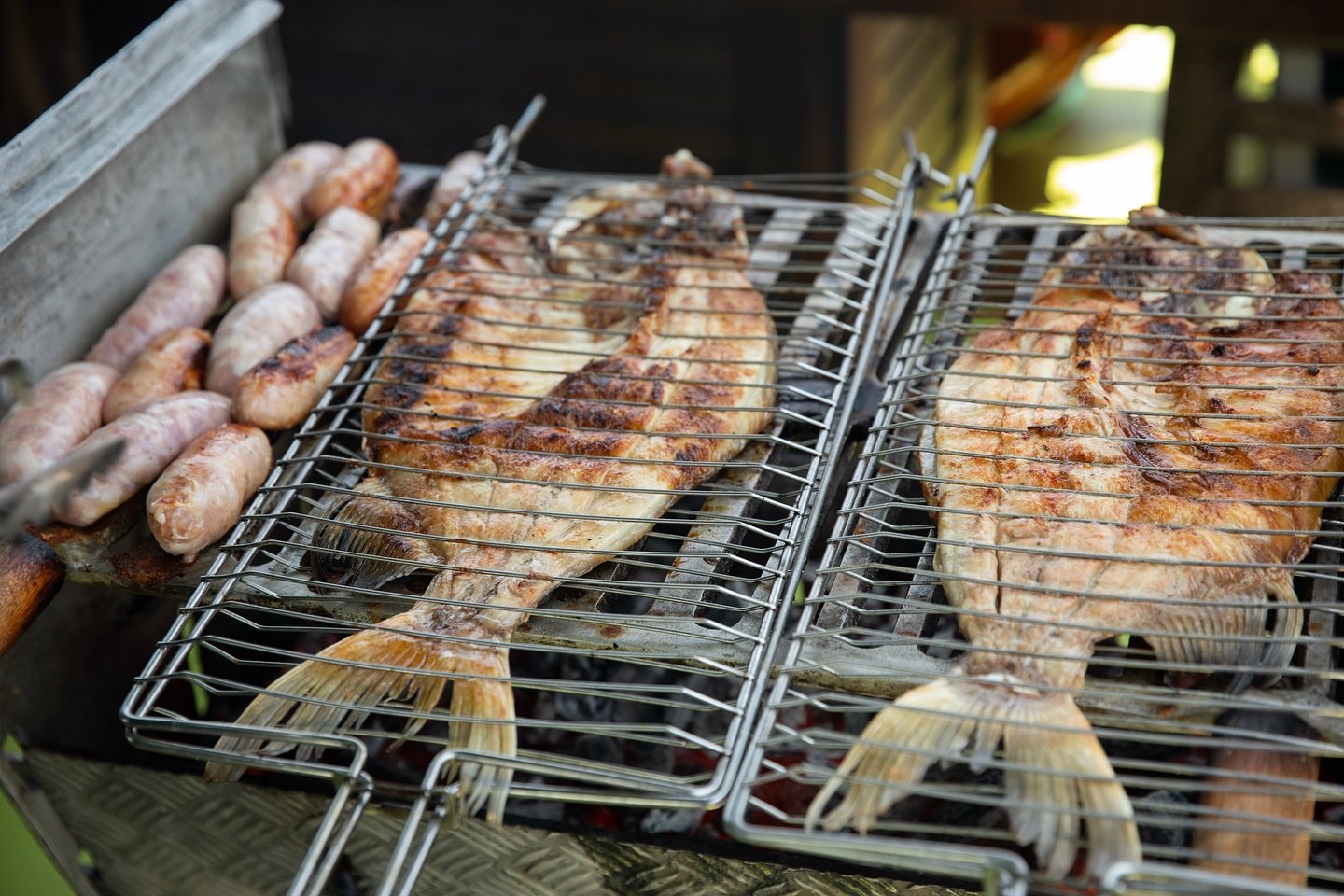 Peixe fresco na brasa, cheiro de mato — almoço amazônico do jeito certo. Peixes inteiros e linguiças sendo grelhados em grelhas de arame sobre carvão em um churrasco ao ar livre