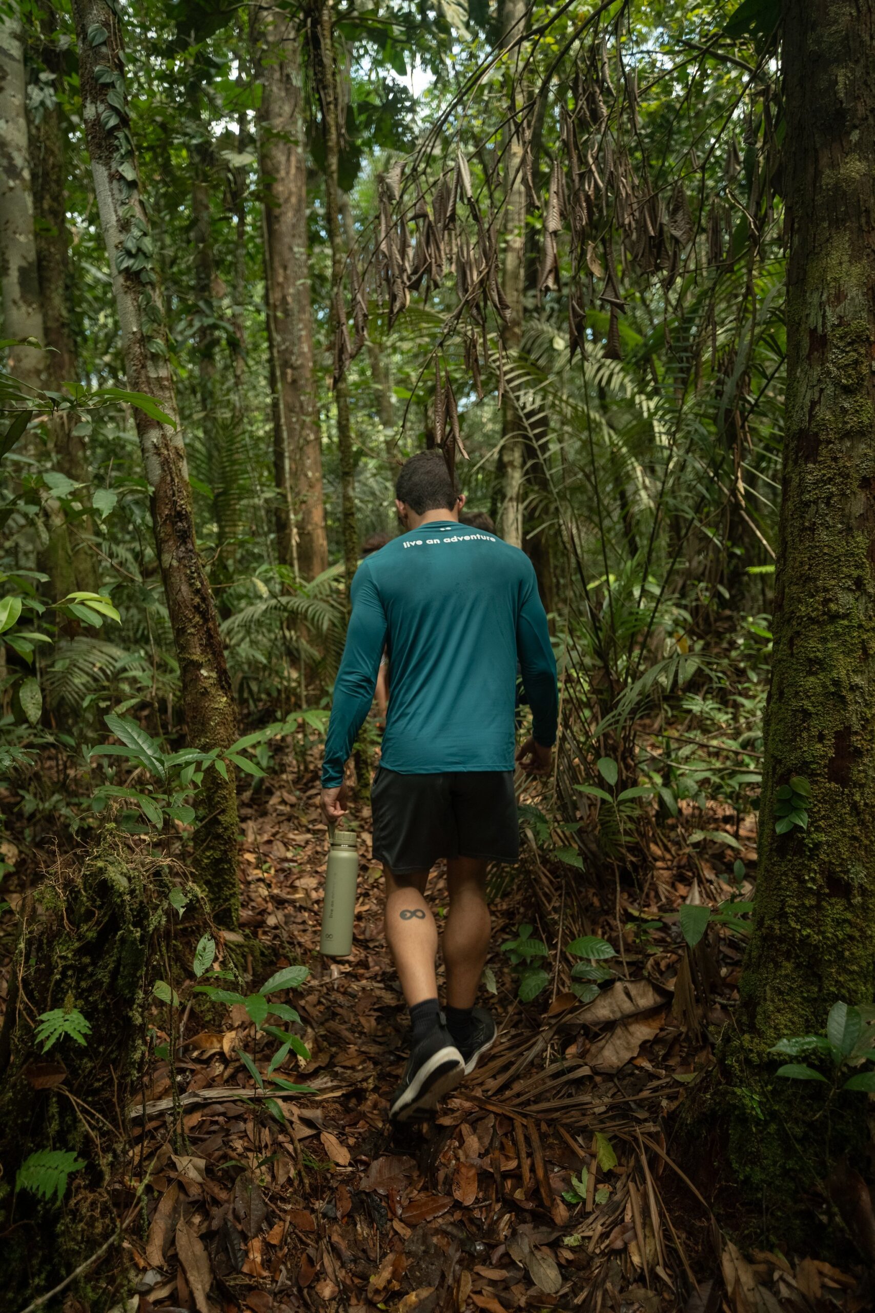 Mata fechada, trilha aberta — a floresta convida você a entrar. Um guia caminha por uma trilha estreita em meio à densa vegetação tropical durante uma excursão de um luxury amazon lodge brazil, carregando uma garrafinha reutilizável