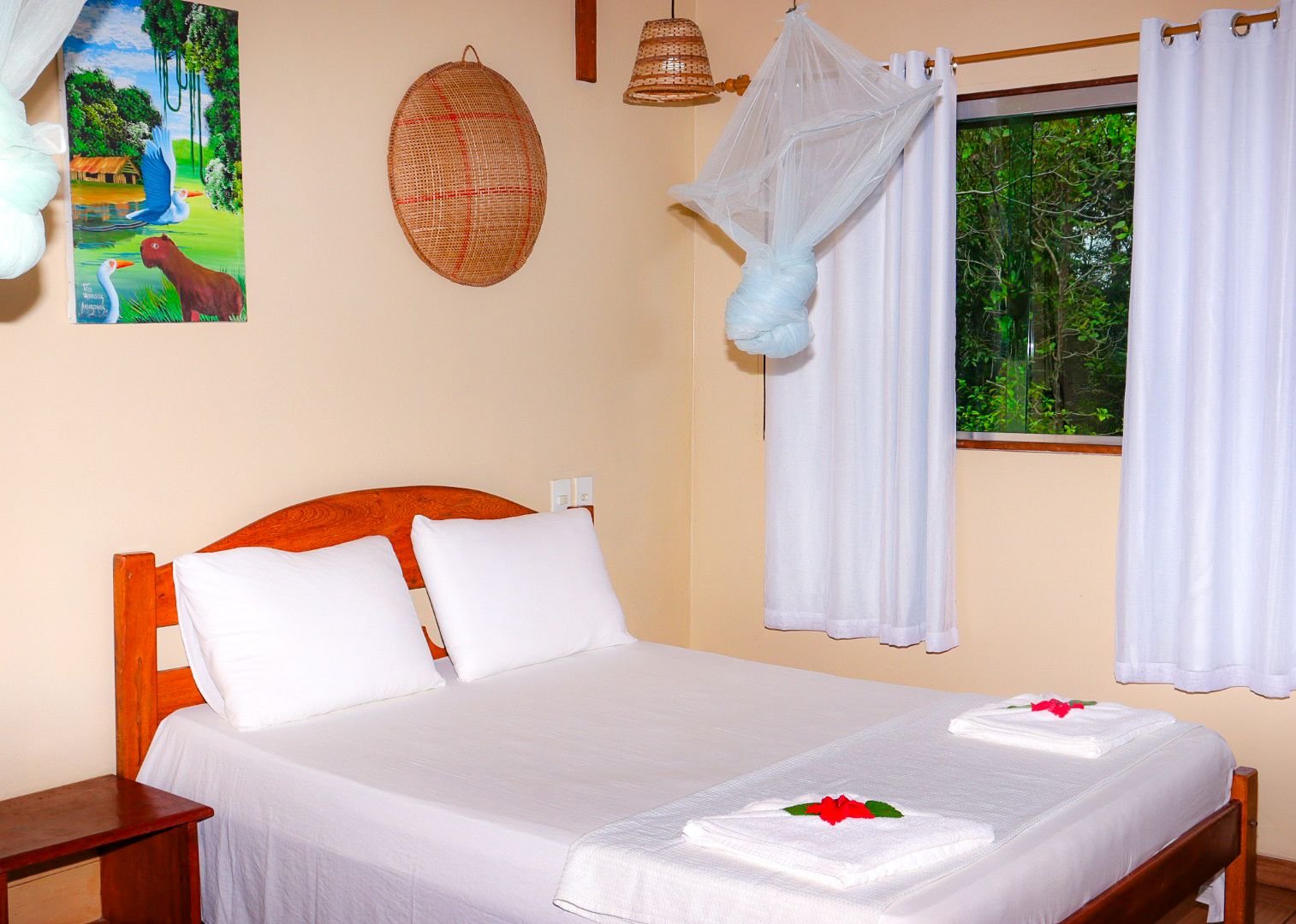 Sunlight and forest views pour through the window beside the comfort bungalow's bed. Masonry comfort bungalow double bed with mosquito net beside a forest-view window in the Amazon
