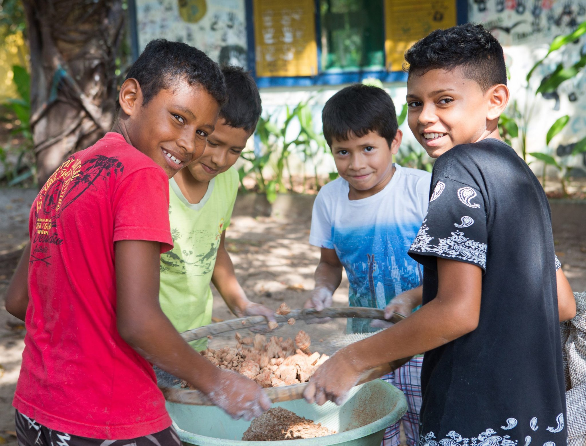 Quatro meninos sorridentes peneiram alimentos juntos em uma tigela grande durante uma visita a uma comunidade ribeirinha perto do Mirante do Gavião na Amazônia