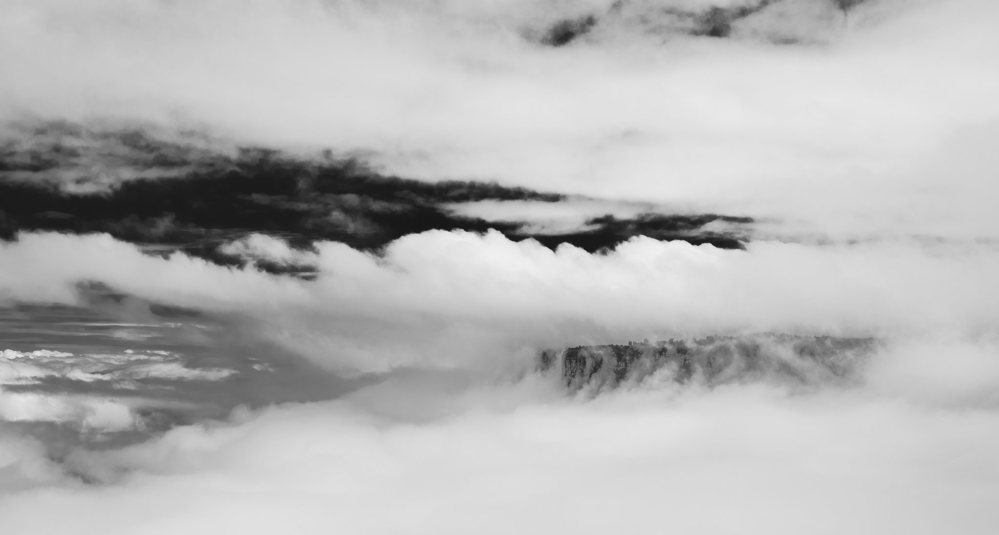 A rocky tepui cliff face barely visible through dense layers of swirling cloud during a Mount Roraima hike, captured in black and white