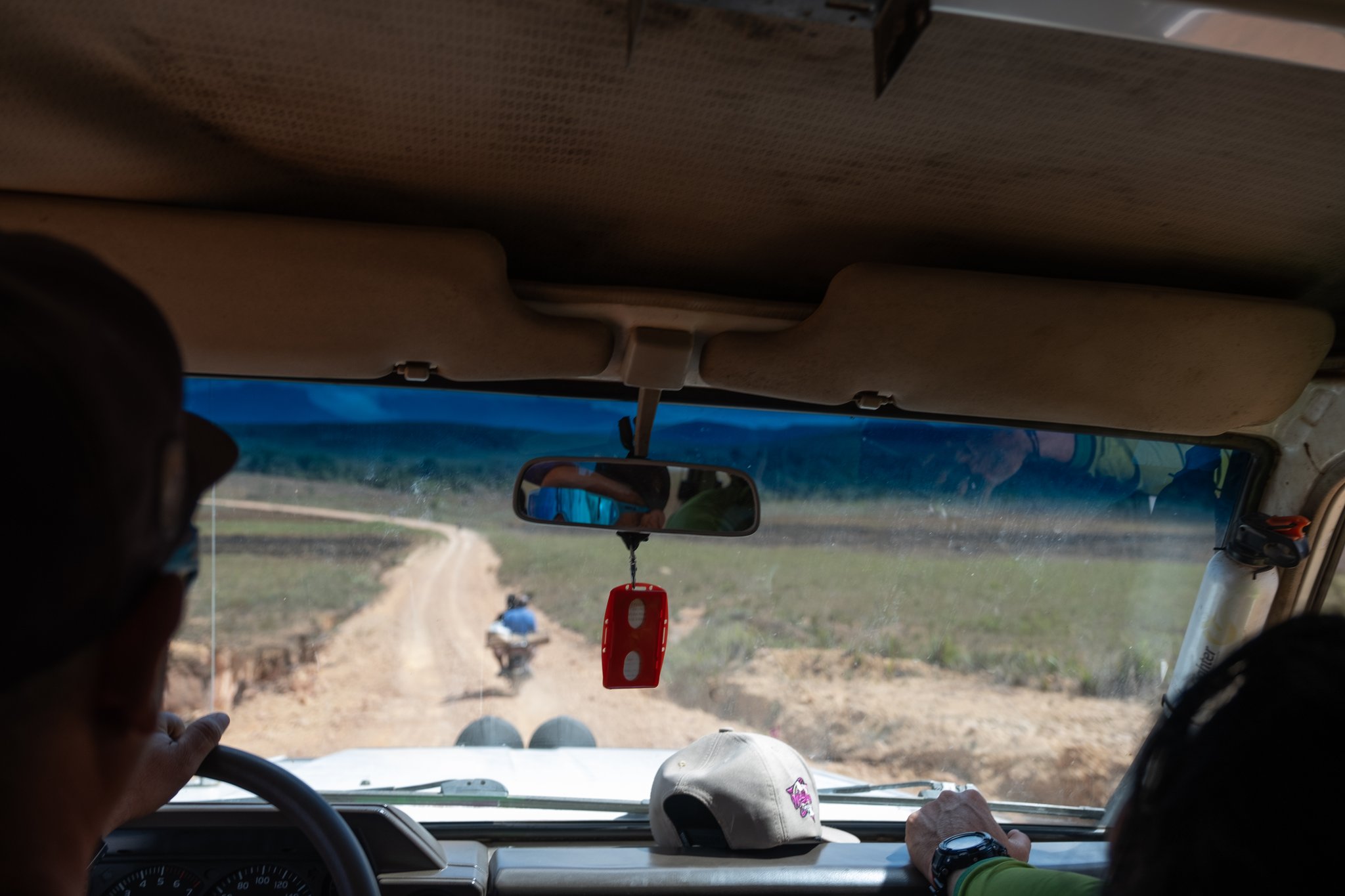 View from inside a 4x4 vehicle on the Mount Roraima trek, following a motorcyclist along a winding dirt track through open savannah grassland