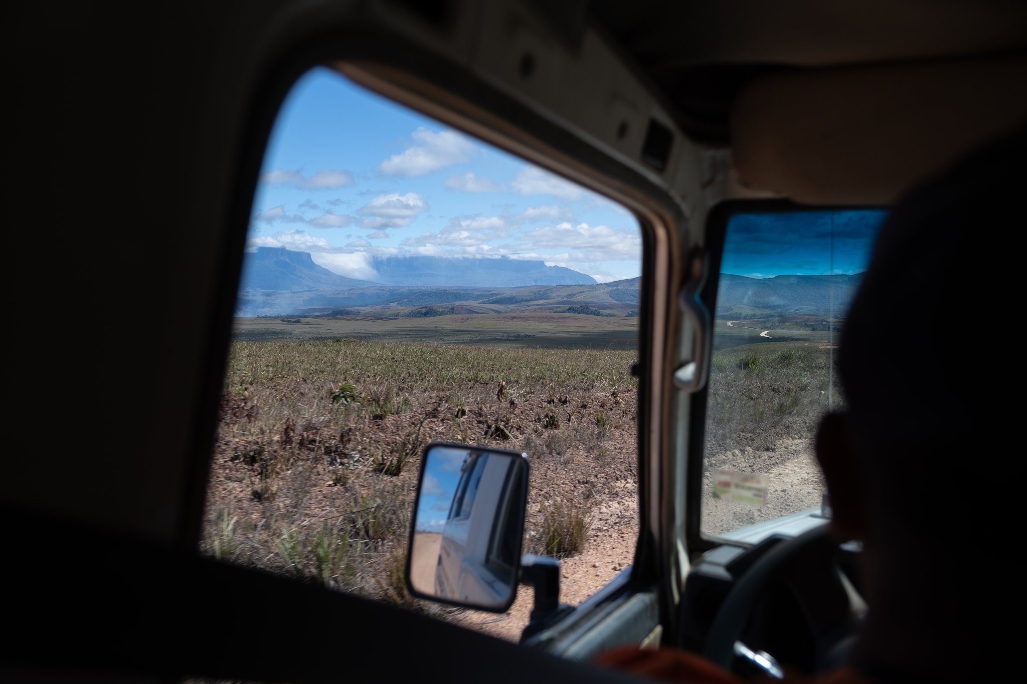 View through a 4x4 vehicle window of a vast open savannah with a flat-topped tepui mesa on the horizon during a Mount Roraima trek approach