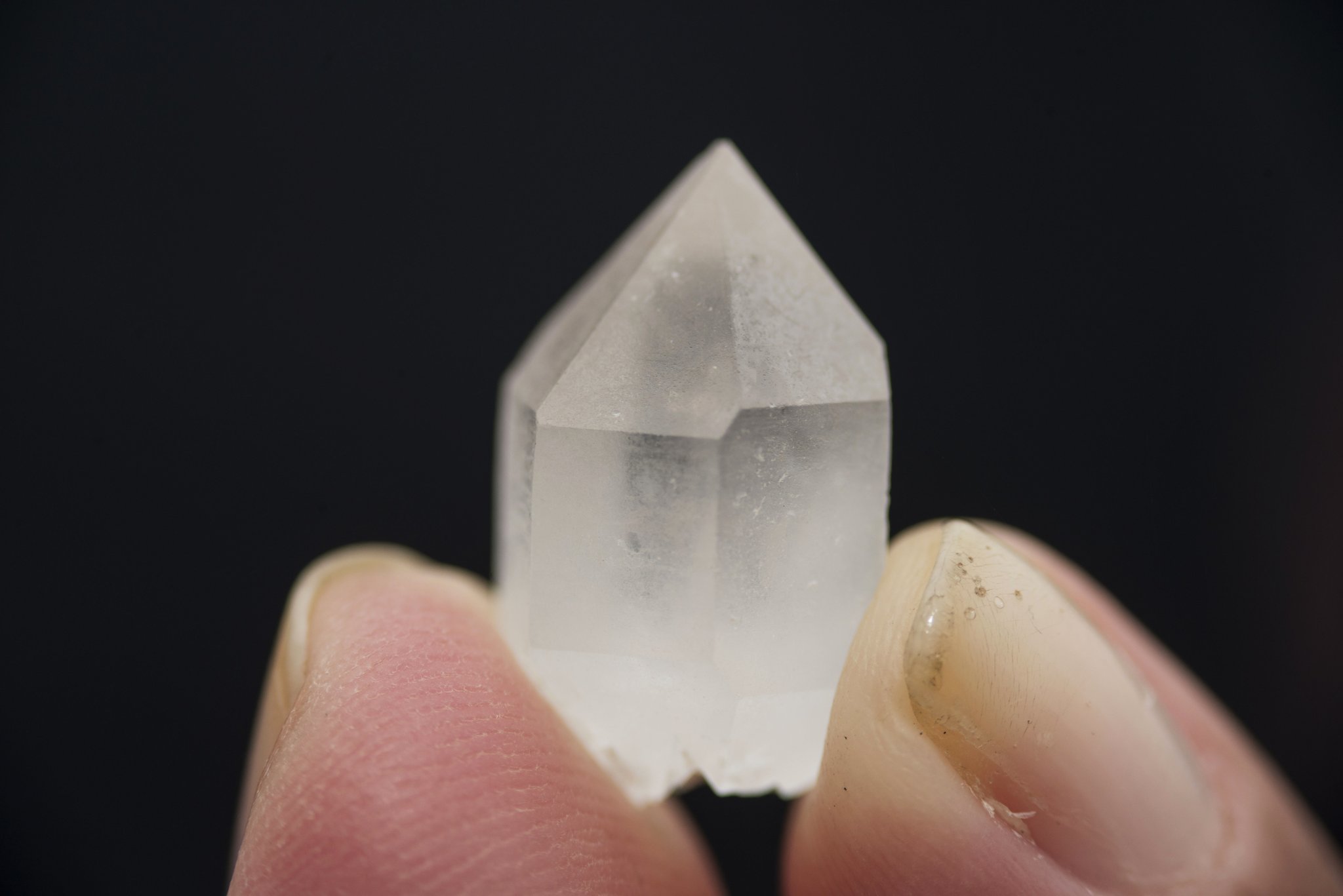 A small clear quartz crystal point held between two fingers against a black background, found during the Mount Roraima trek through the Valley of Crystals