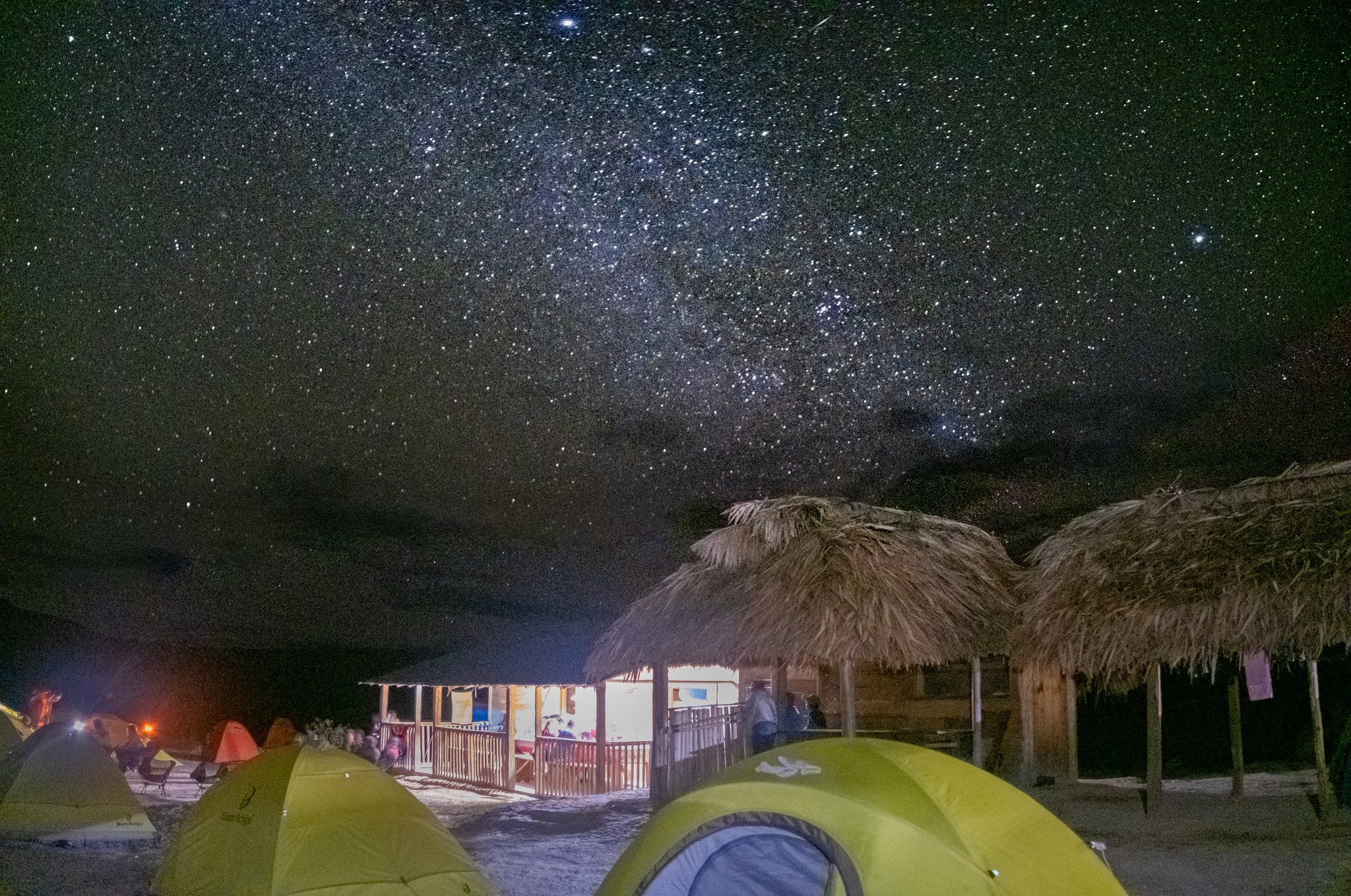 Green dome tents and thatched-roof shelters at a remote campsite on the Mount Roraima trek, beneath a brilliant Milky Way filling the night sky
