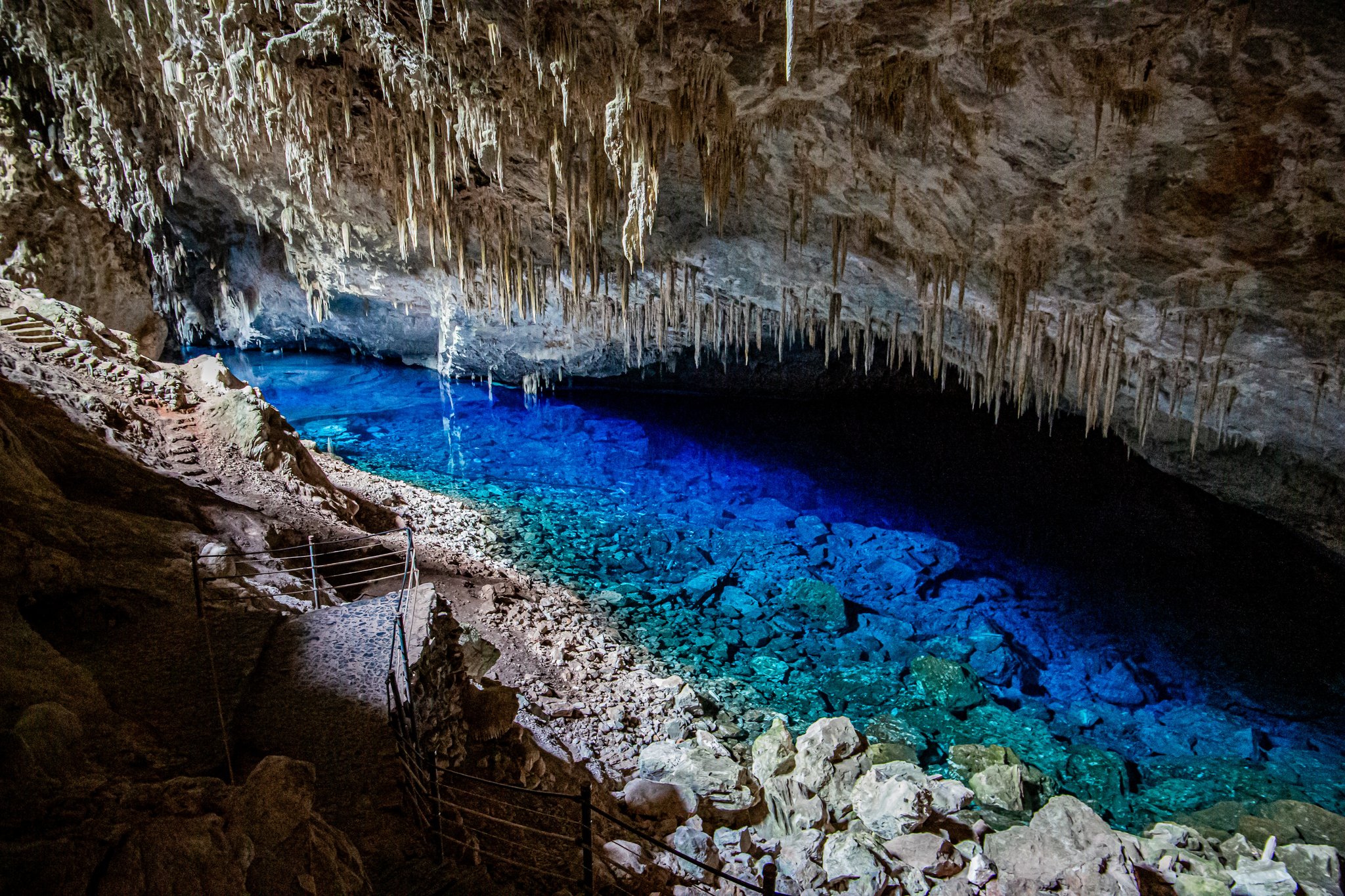 Stalactites by the thousands, a lake that glows electric blue — and absolute silence underground. Photo: Bruno Wagner A glowing turquoise underground lake inside a limestone cave on a Pantanal Bonito tour, with dense stalactites hanging from the ceiling and a narrow viewing path along the rocky shore