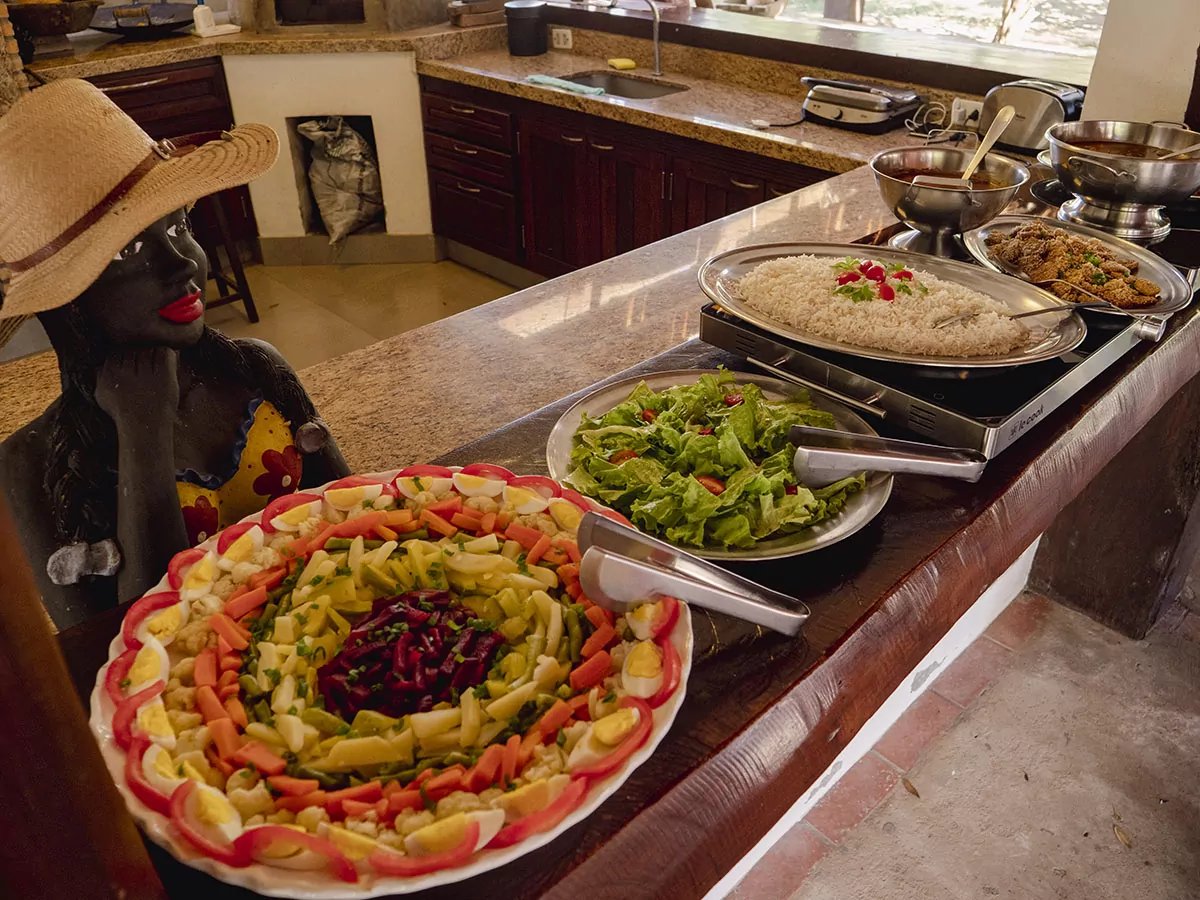 Fresh, colorful and generously laid out — lunch at the lodge. A colorful lodge buffet on a Pantanal Bonito tour featuring a decorative salad platter with boiled eggs, carrots and beetroot, alongside rice, green salad and breaded dishes on a granite counter, with a traditional ceramic figure nearby