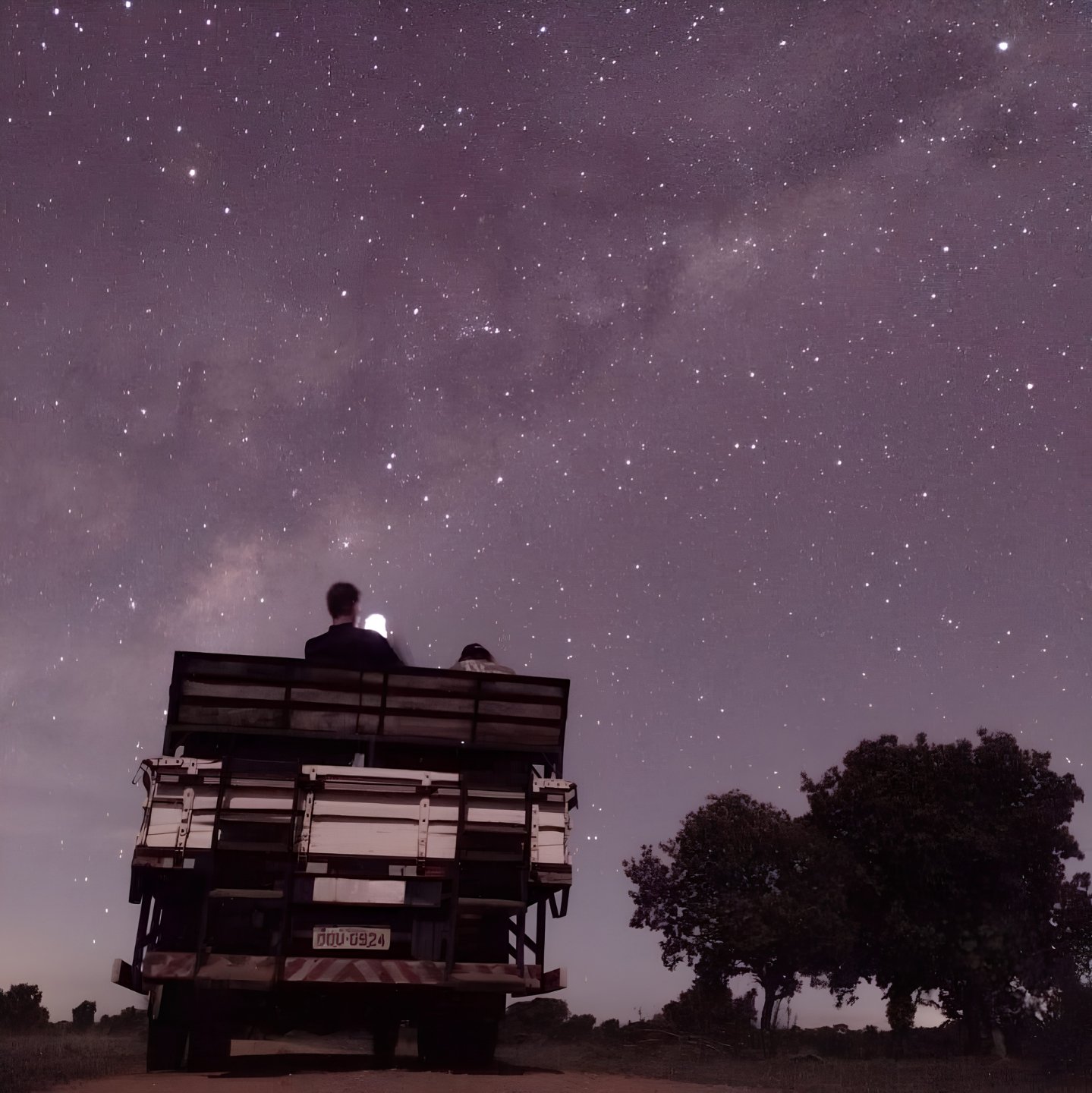 Millions of stars, zero light pollution — the night sky opens up on the road to the Pantanal. Two travelers sitting on the back of an open safari vehicle beneath a vast star-filled sky and visible Milky Way on a Pantanal Bonito tour night safari