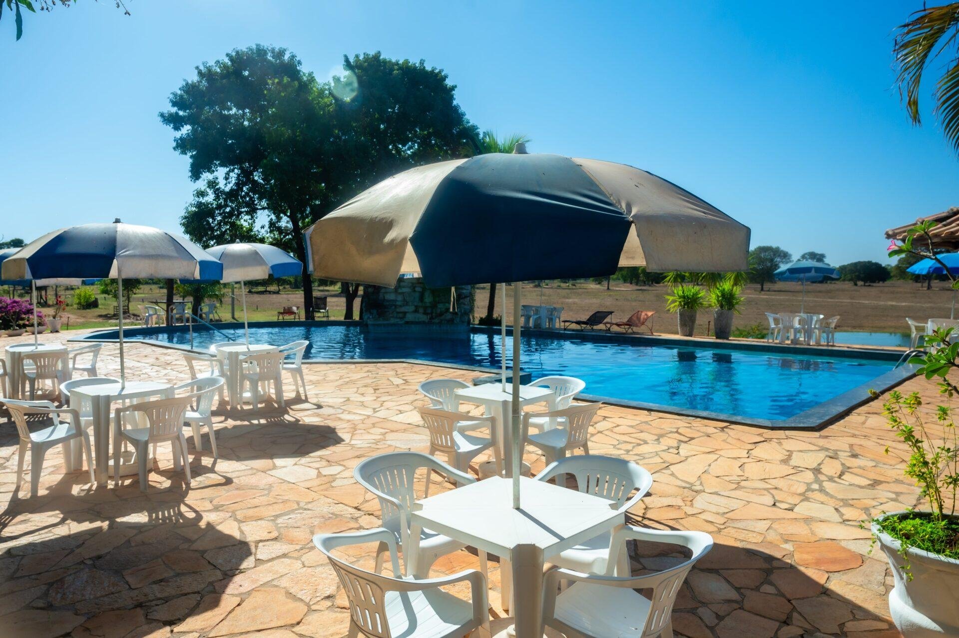 Stone-paved terrace, open skies, and a cool pool waiting after a morning on the water. Sunny outdoor pool terrace with white tables, chairs, and striped umbrellas at a lodge on a pantanal jaguar budget safari
