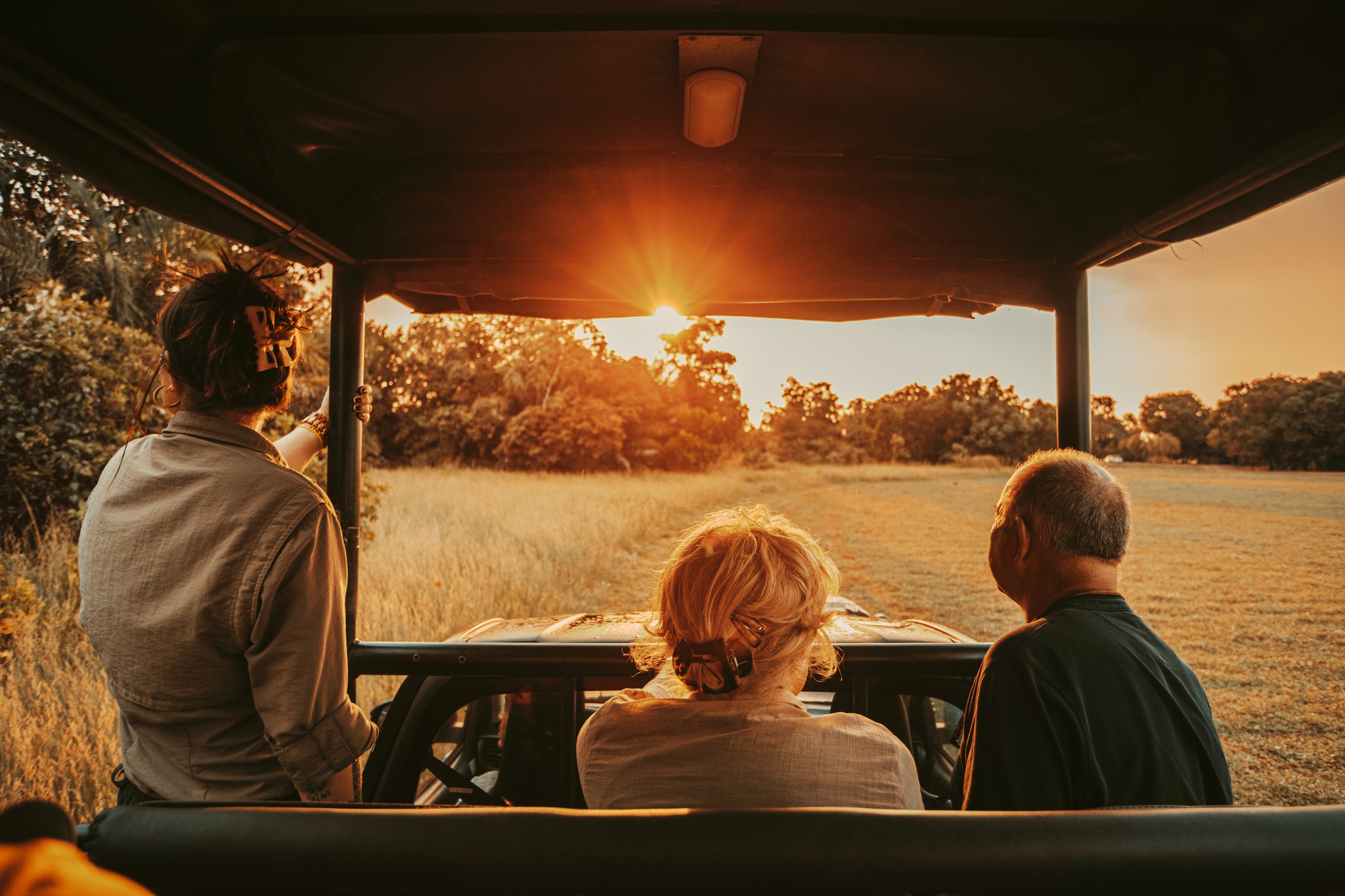 Three guests aboard an open safari vehicle watching a blazing golden sunset over open grassland and tree line during a pantanal luxury safari