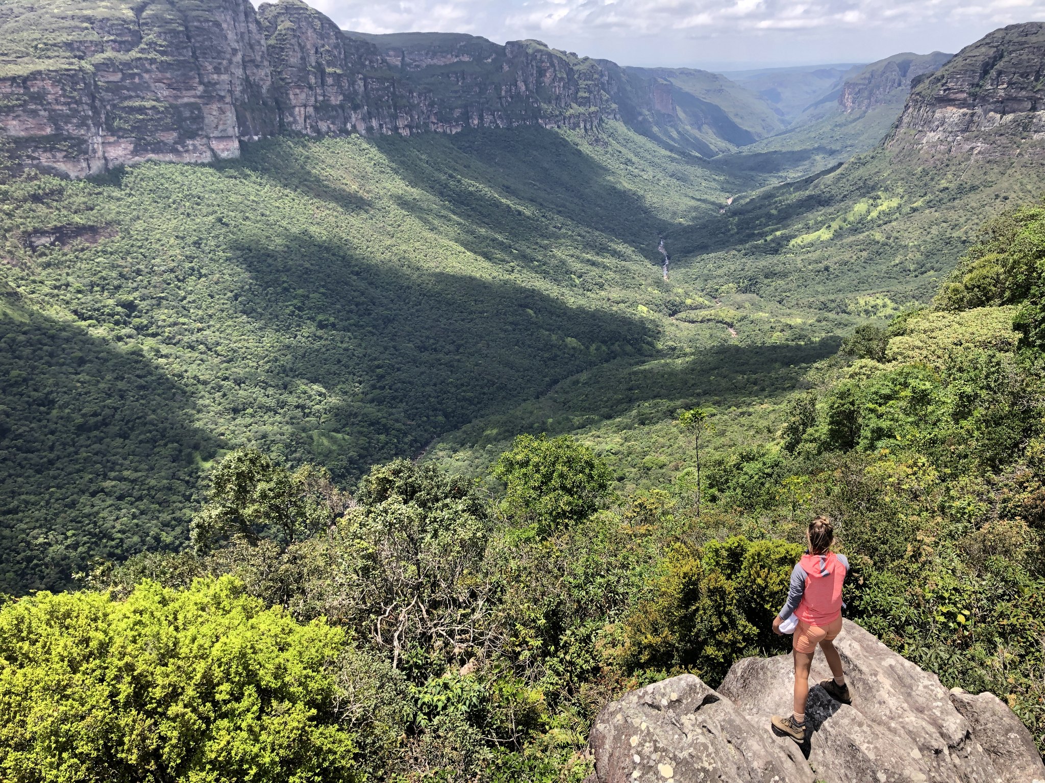Every step up earns this — an endless green canyon stretching to the horizon. Photo: Lucas Neves A hiker stands on a rocky outcrop overlooking the vast forested canyon of the Pati Valley hike, with sheer sandstone cliffs and a distant waterfall visible in the valley below