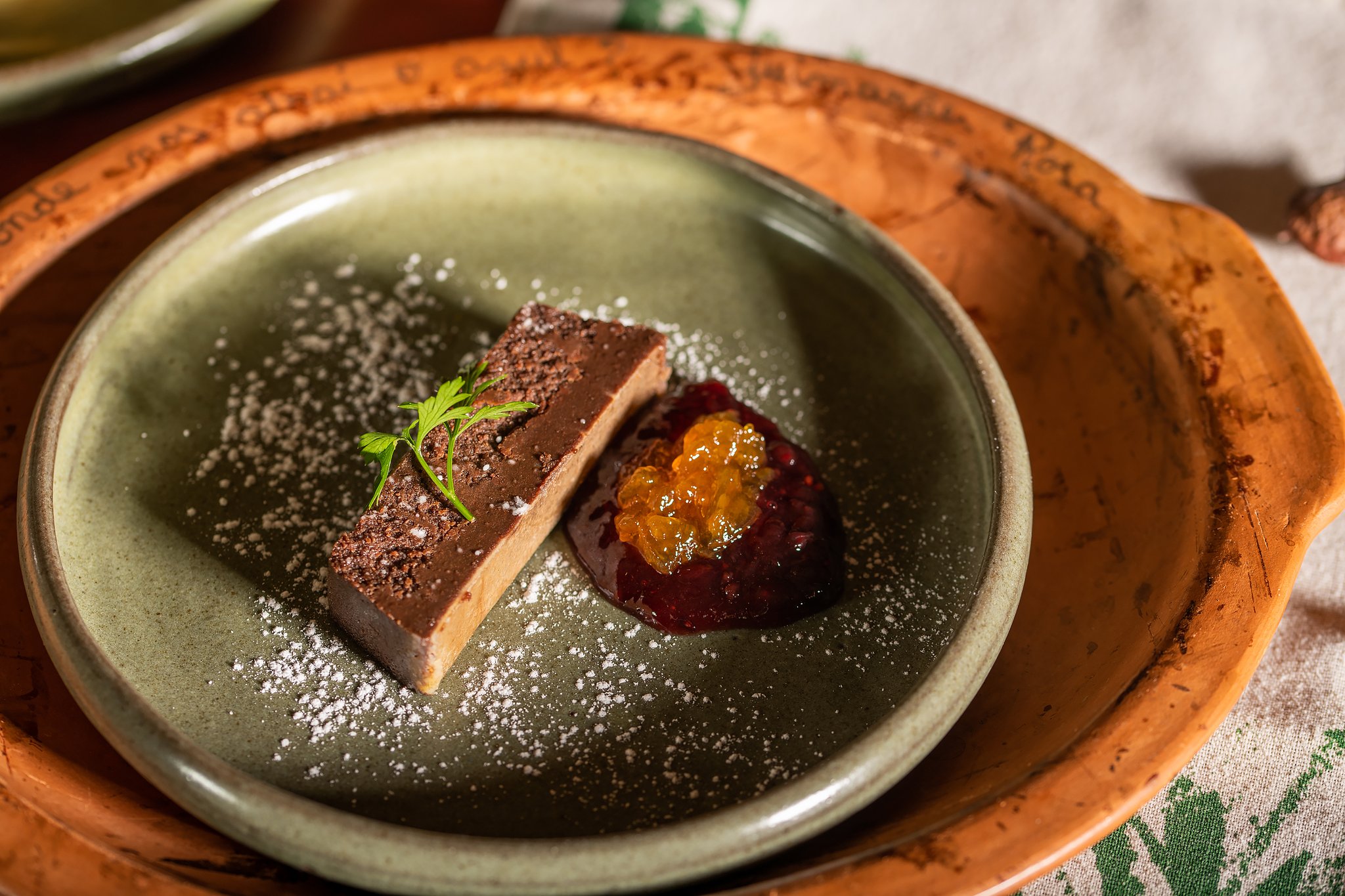 Farm-fresh flavours, artfully plated — dining at Pousada Trijunção is as memorable as the wildlife. Plated chocolate terrine slice dusted with cocoa powder and icing sugar, served alongside a jewel-toned fruit compote with golden caviar pearls on a sage-green ceramic plate at Pousada Trijunção