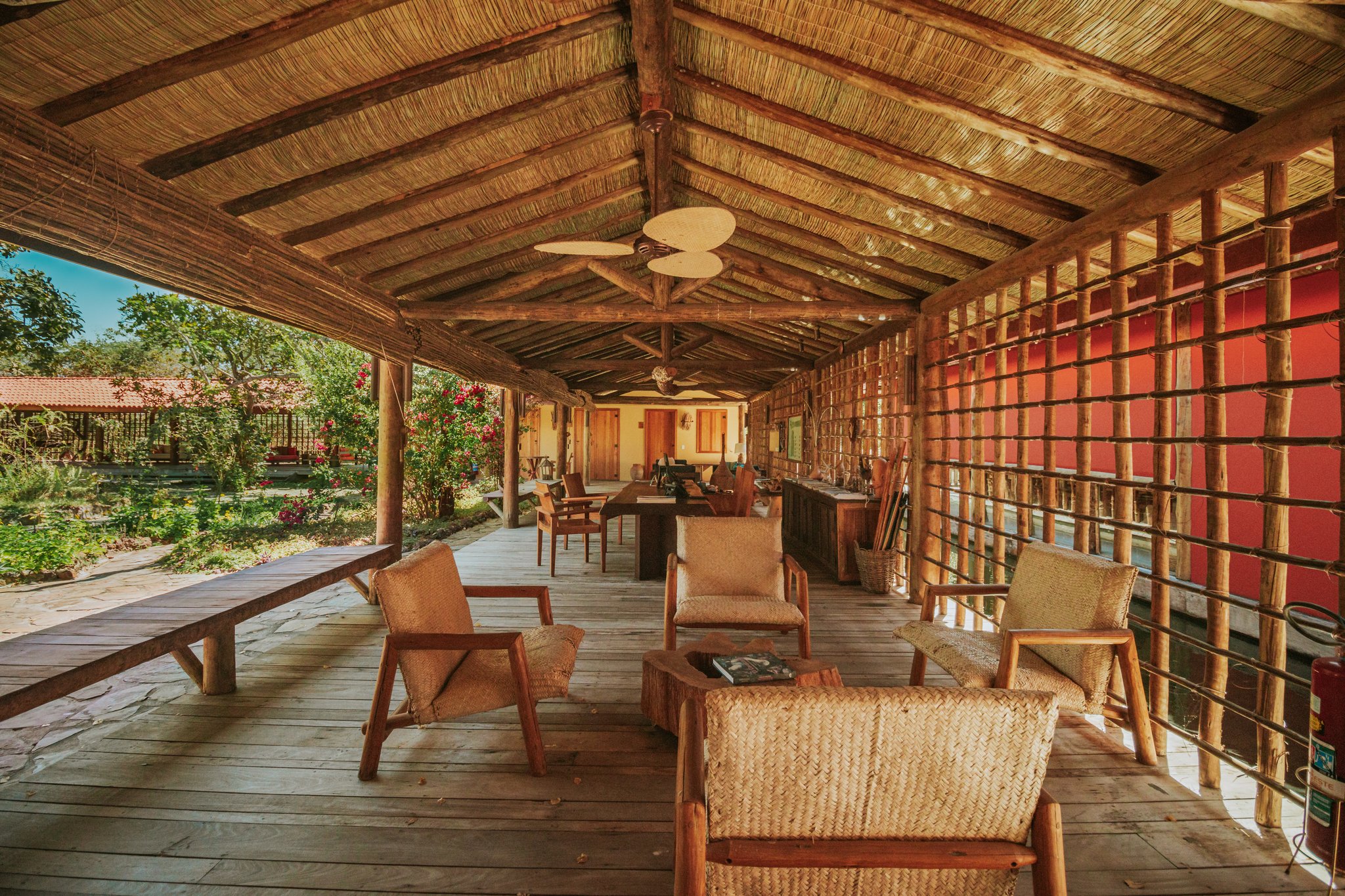 Unwind on the terrace as the Cerrado afternoon light floods through the palms. Photo: Albori Ribeiro Open-air lounge terrace at Pousada Trijunção with woven rattan chairs, rustic wooden deck, thatched palm roof and a lush garden view