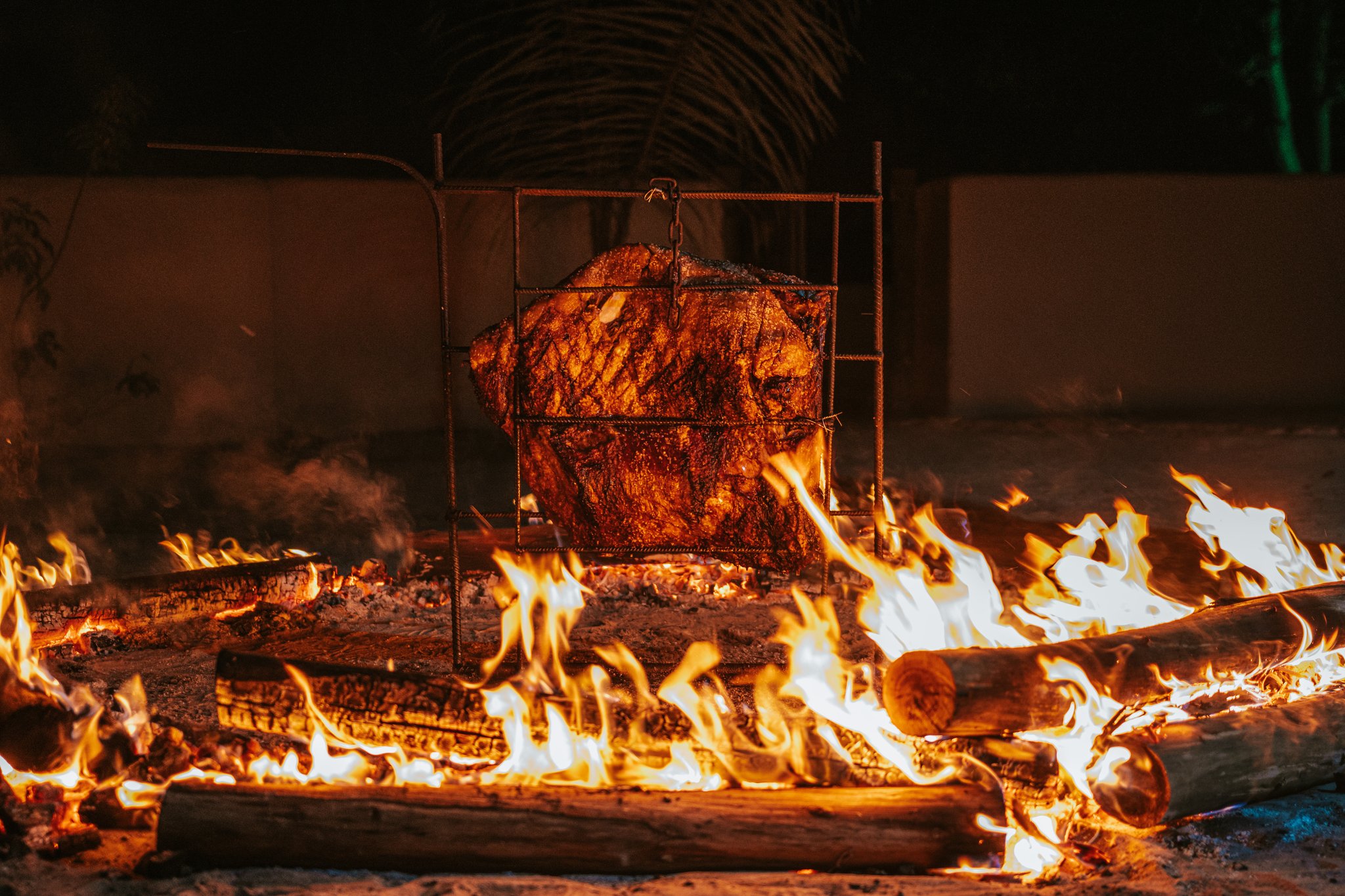 Fire-roasted and unhurried — evenings at Trijunção taste like the wild Cerrado itself. Photo: Albori Ribeiro A large cut of meat slow-roasting in a rustic iron cage grill over open wood flames at night at Pousada Trijunção, deep in the Cerrado