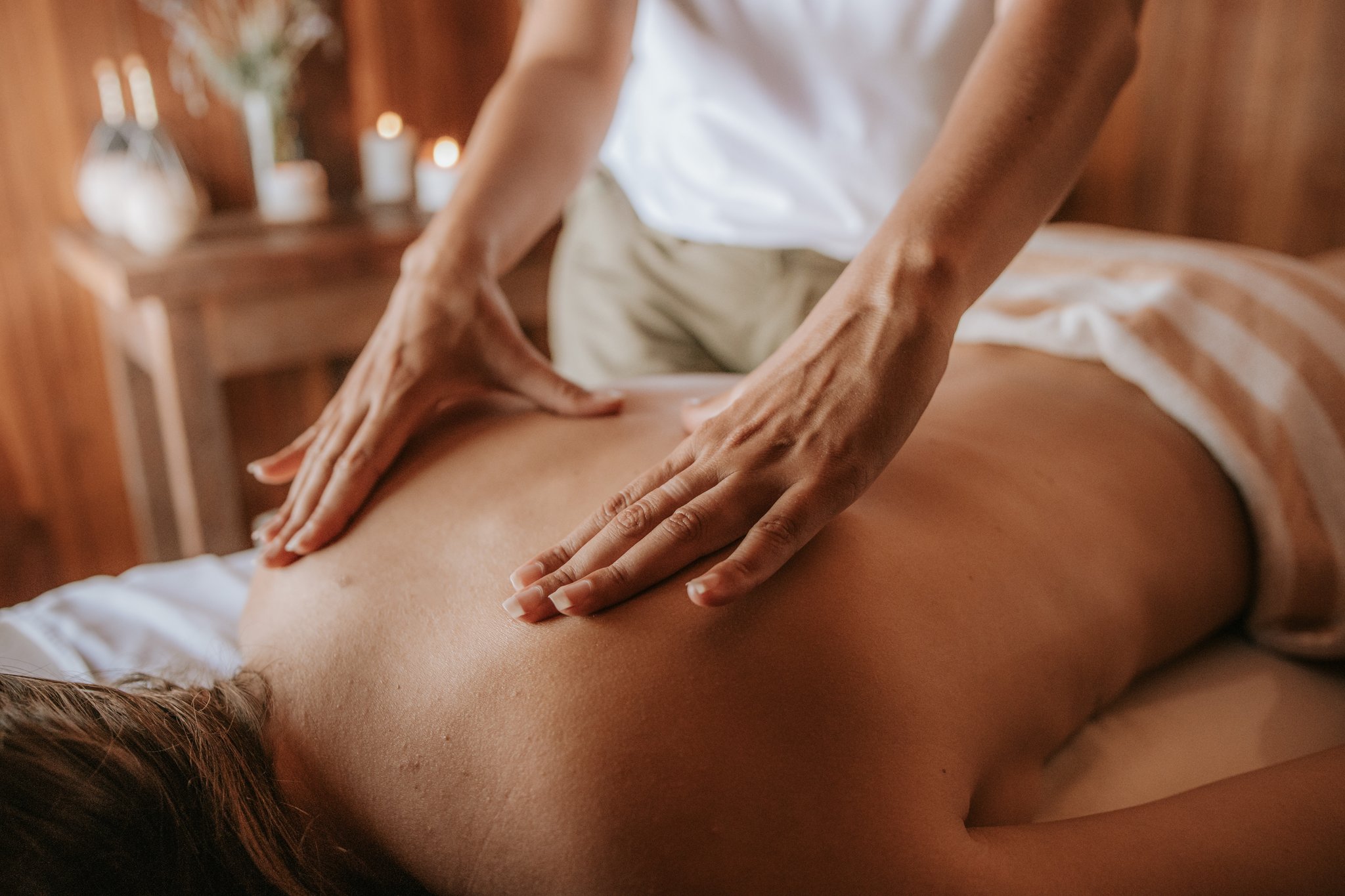 A therapist performing a relaxing back massage by candlelight in the warm wooden spa room at Pousada Trijunção