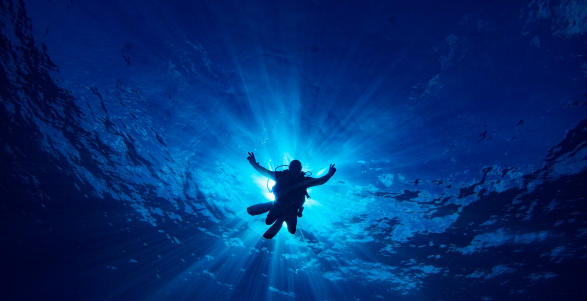 Scuba diver silhouetted against sunbeams underwater during an Open Water diving course in Fernando de Noronha