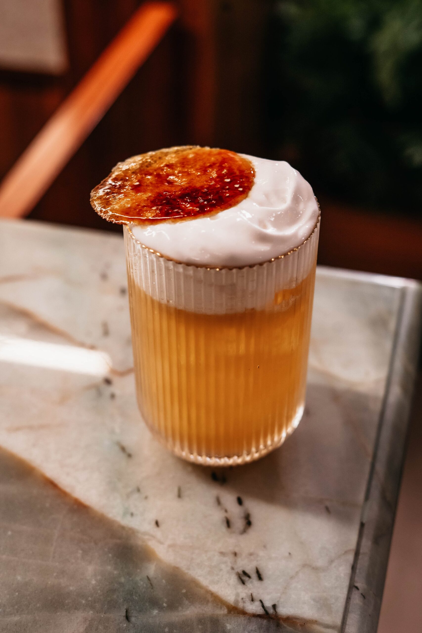 A ribbed glass filled with an amber cocktail, topped with thick white foam and a caramelised brûléed disc, served aboard the untamed amazon cruise