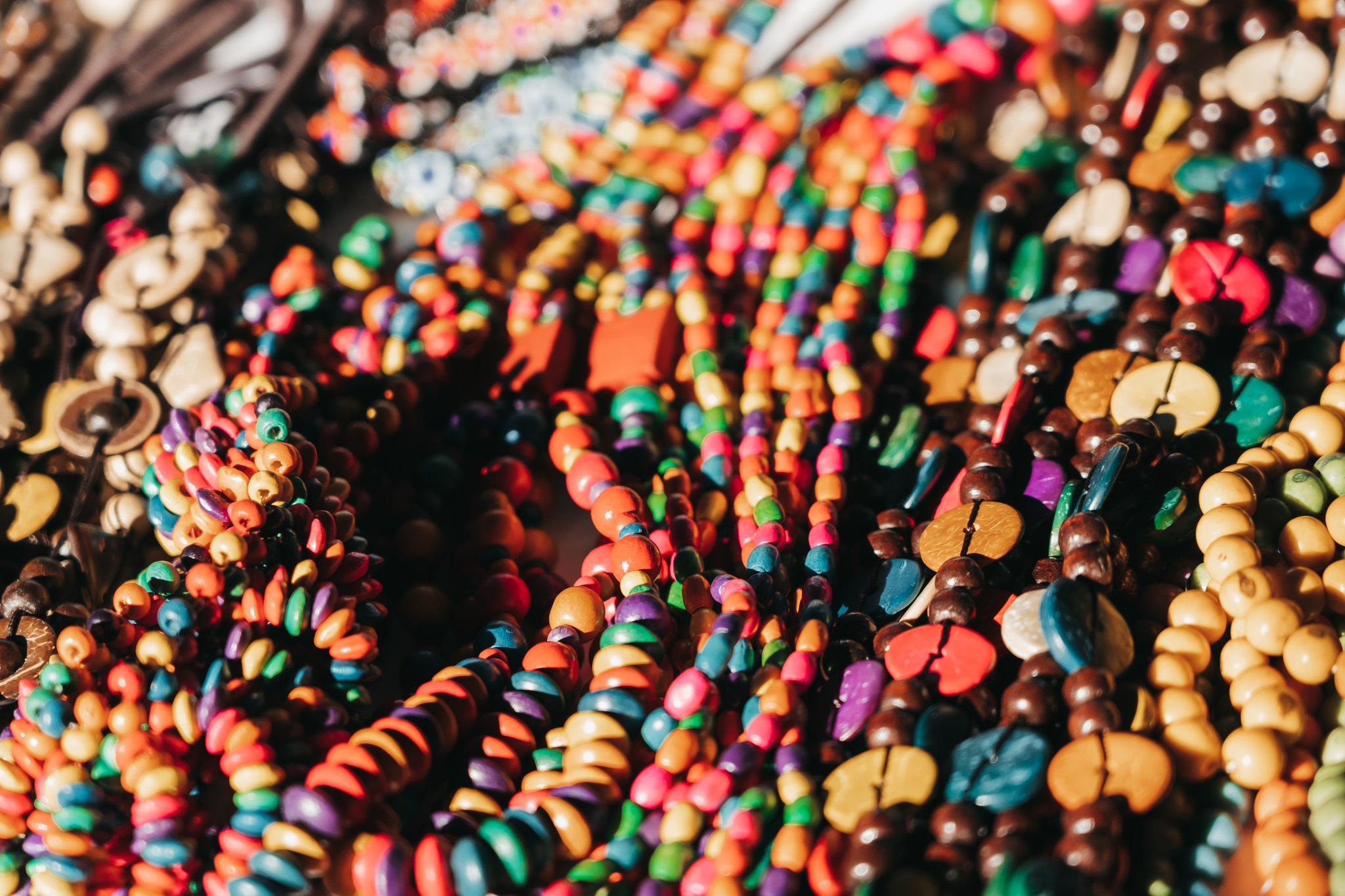 A dense display of multicolored wooden and seed bead necklaces and bracelets at a local artisan market, showcasing handcrafted souvenirs from the untamed Amazon cruise region
