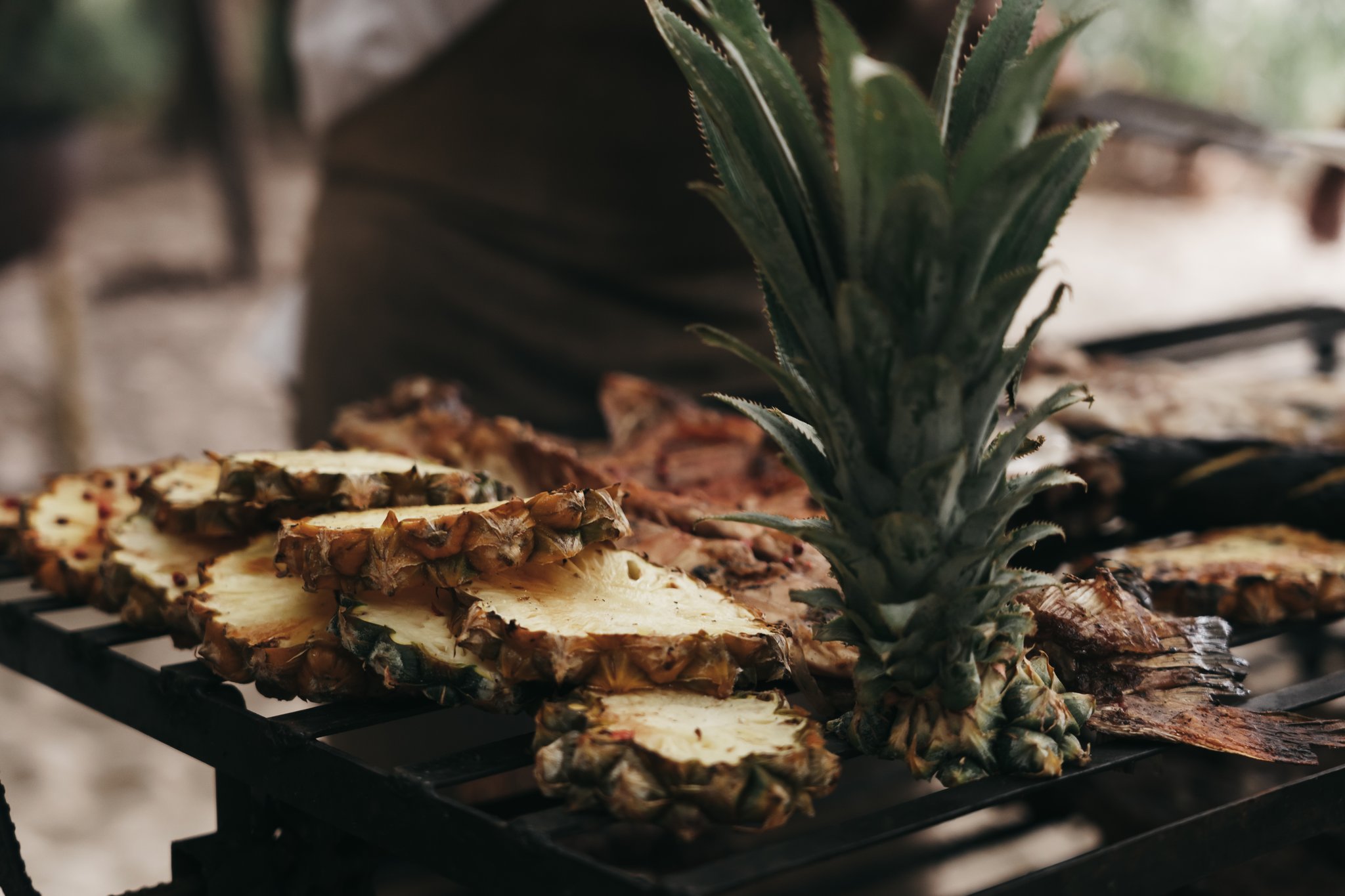 Halved pineapple with its crown intact resting on a dark outdoor grill grate alongside caramelised slices, served during the untamed amazon cruise