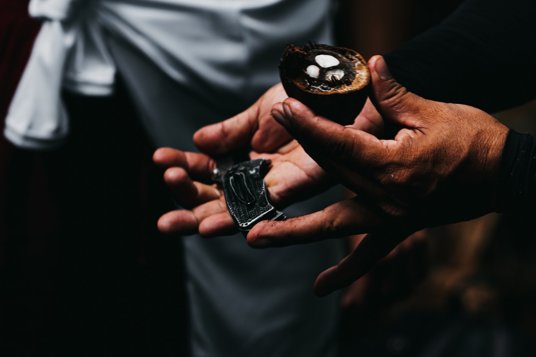 Weathered hands holding a halved tucumã palm nut and a small folding knife during a community visit on the untamed amazon cruise