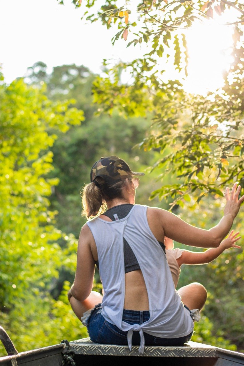 First contact with the forest: light filters through and the jungle comes alive. Woman seen from behind reaching toward sunlit green jungle foliage