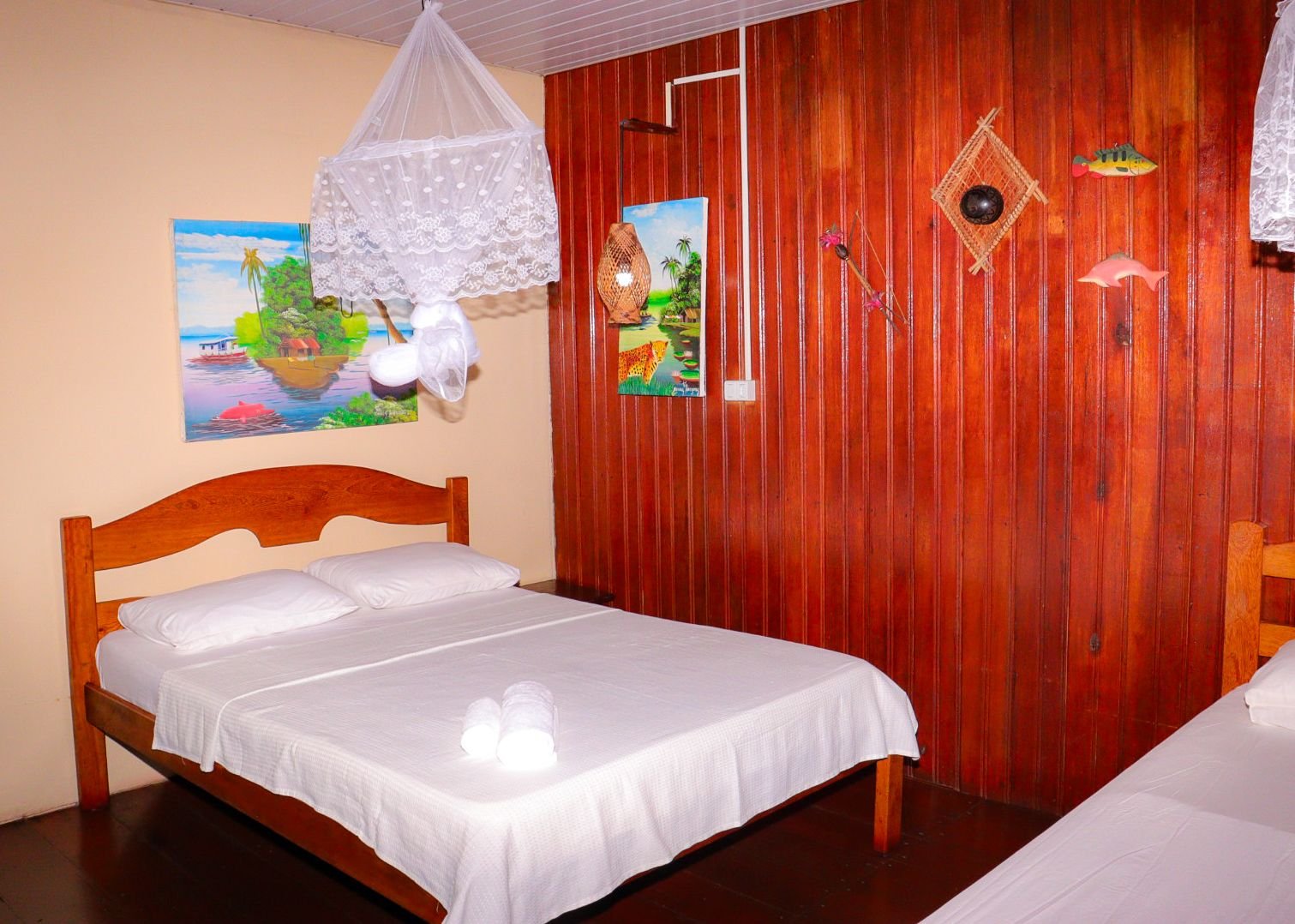 Inside, warm wood panelling and a mosquito net keep the bungalow snug. Cozy wooden bungalow room with a double bed, mosquito net and local art on red wood-panel walls